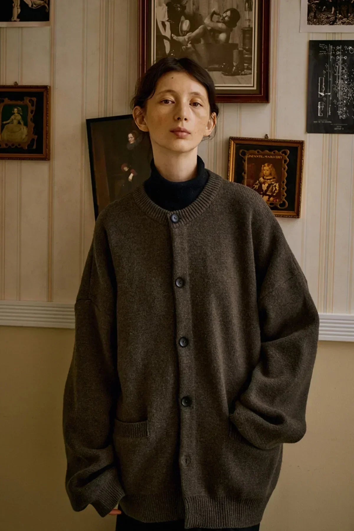 Person wearing oversized brown cashmere cardigan with buttons and front pockets in vintage room
