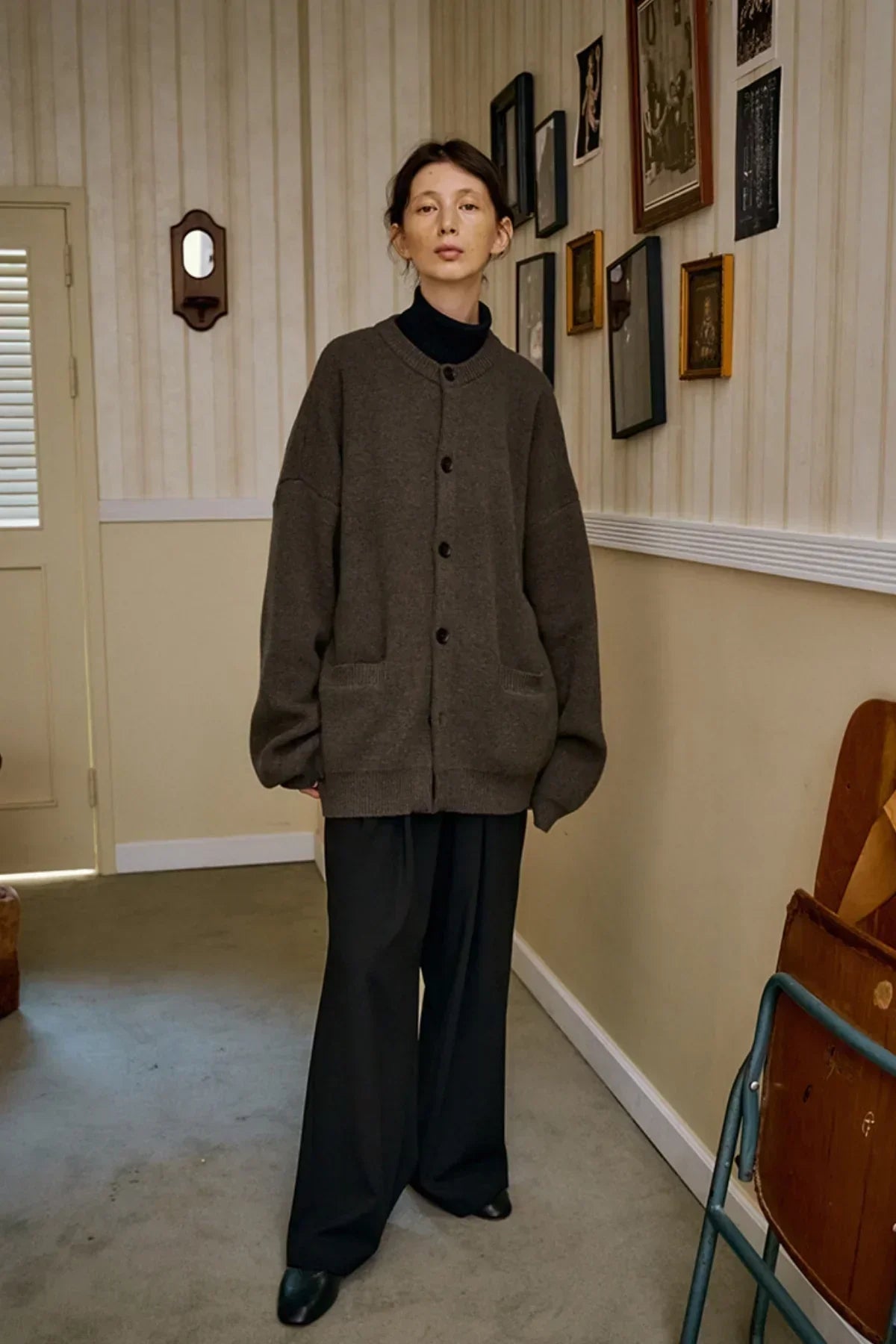 Model wearing oversized brown cashmere cardigan and black wide-leg pants in vintage room