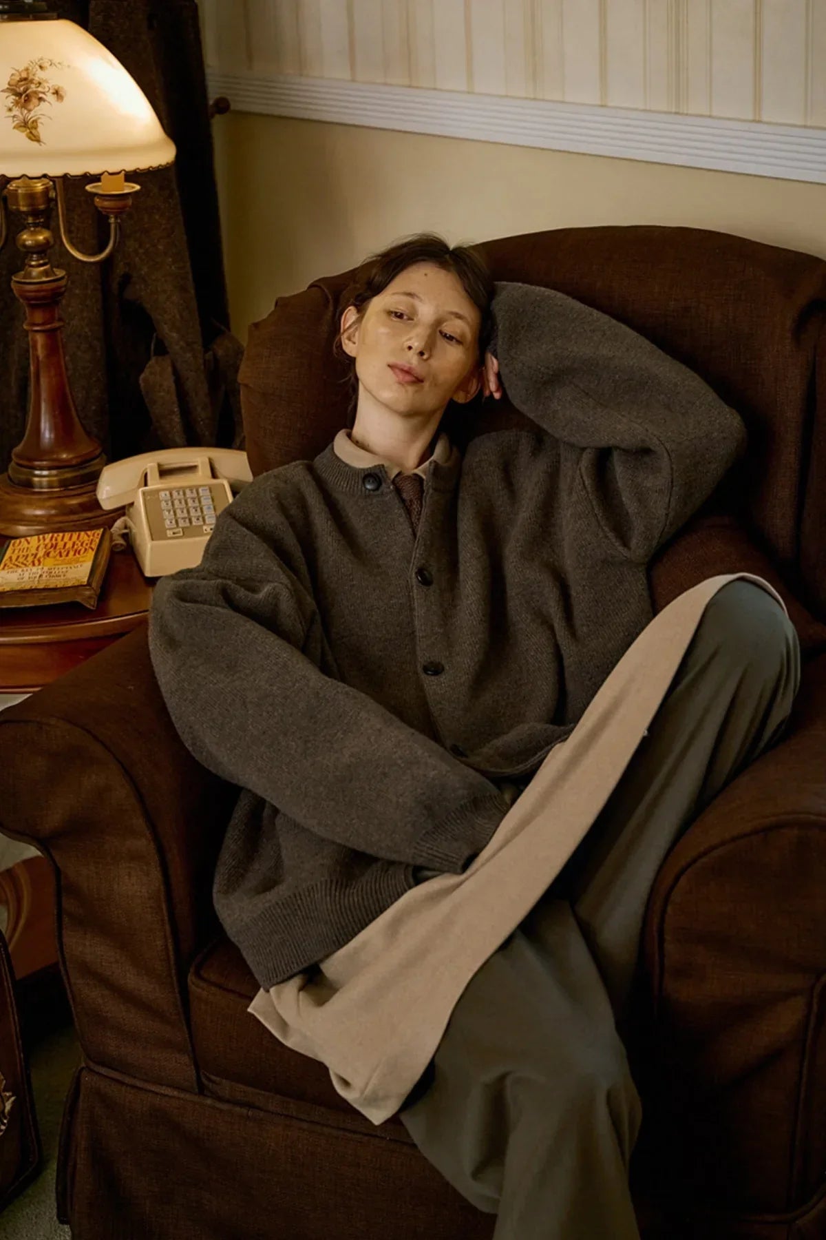 Person wearing oversized dark brown cashmere cardigan sitting on brown armchair in cozy vintage room