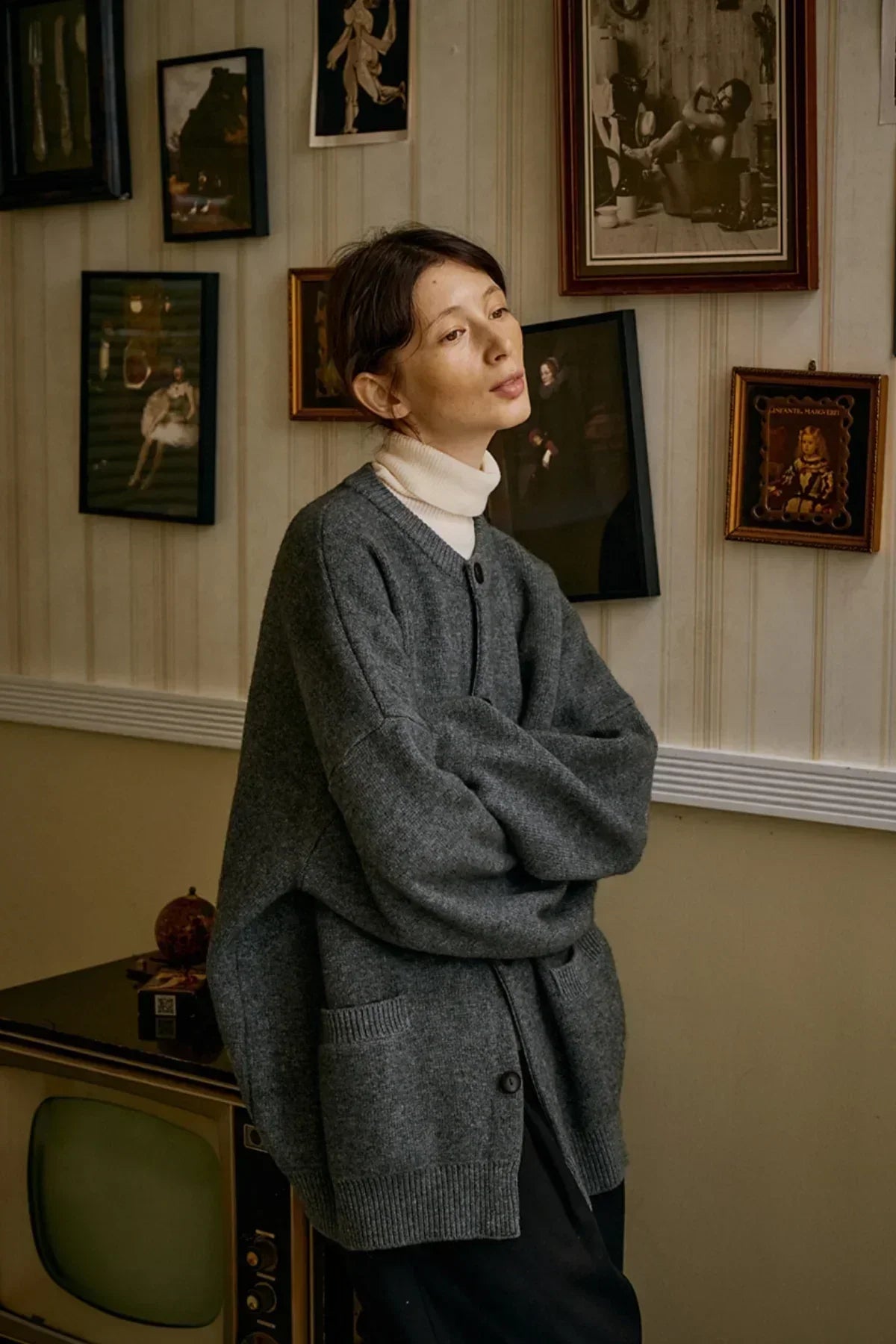 Woman wearing oversized gray cashmere cardigan with pockets over white turtleneck in vintage room
