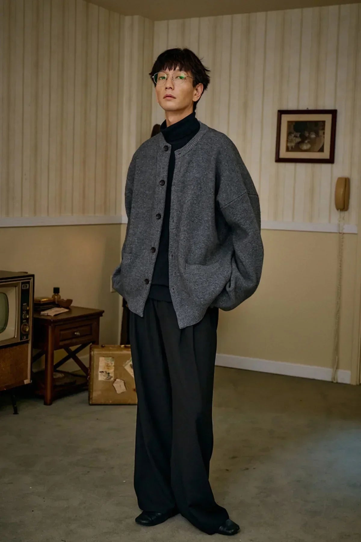 Model wearing a gray unisex cashmere cardigan with black turtleneck and wide black pants in vintage room