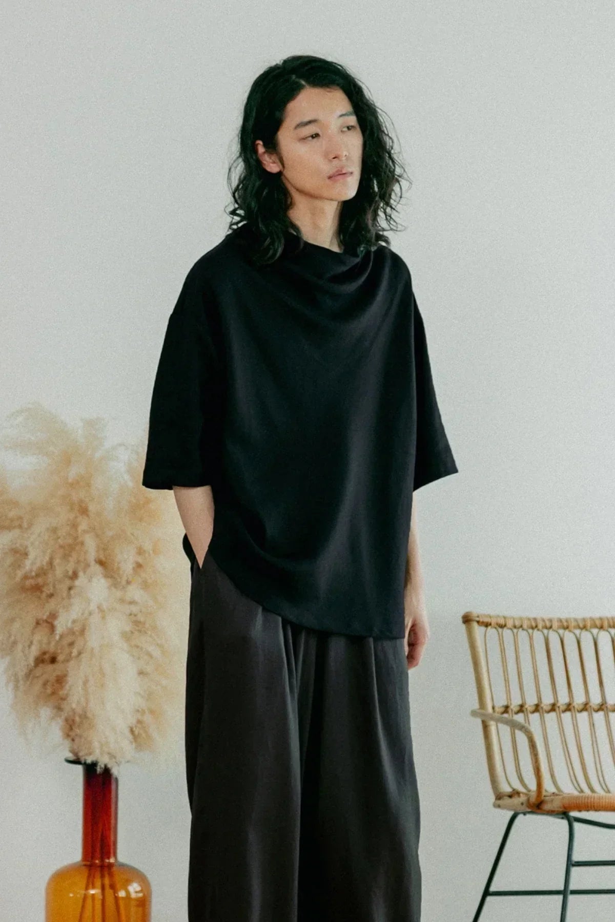 Person wearing black unisex cowl neck t-shirt with loose sleeves and dark pants indoors