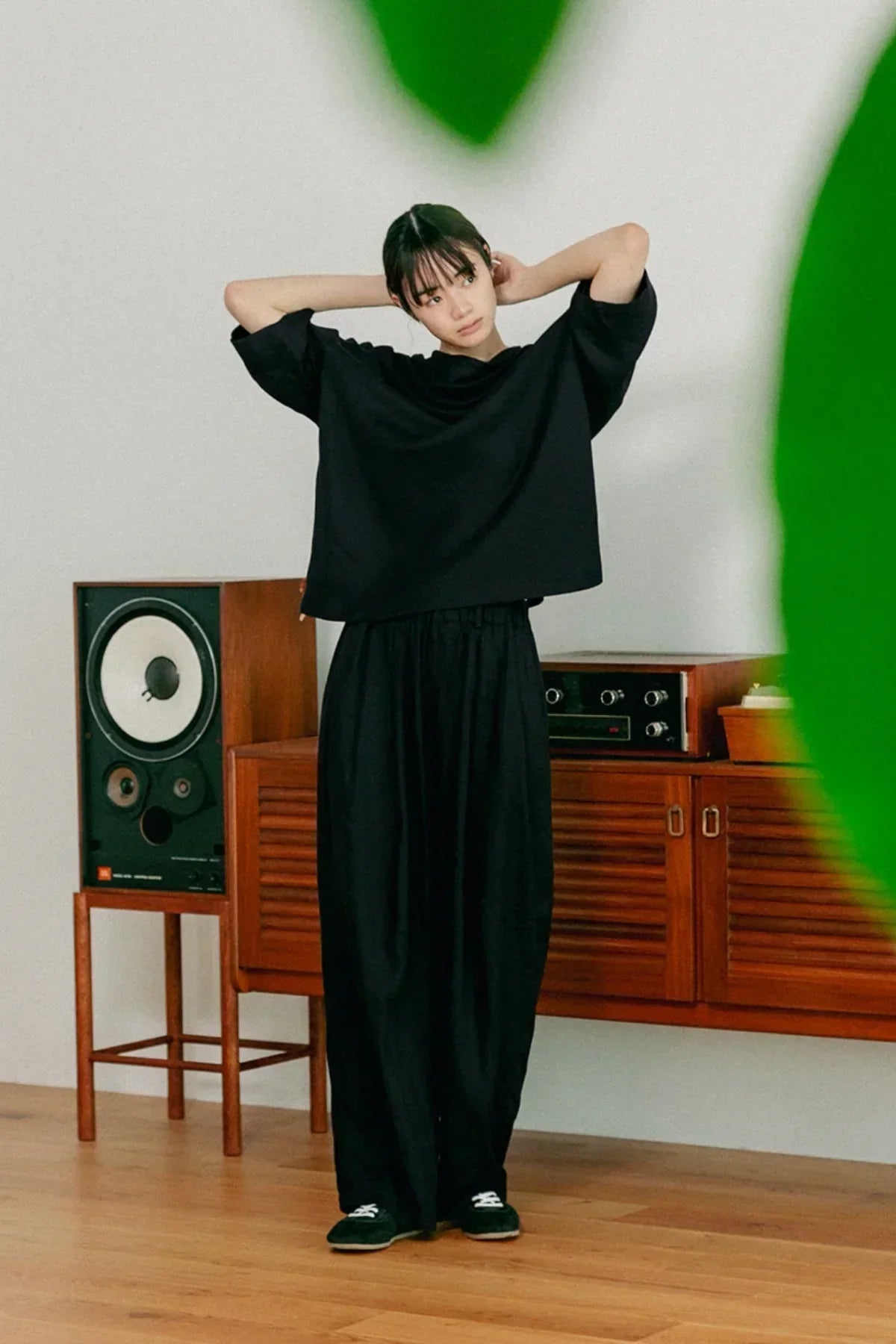 Model wearing black unisex cowl neck t-shirt and loose pants in stylish room with wooden furniture
