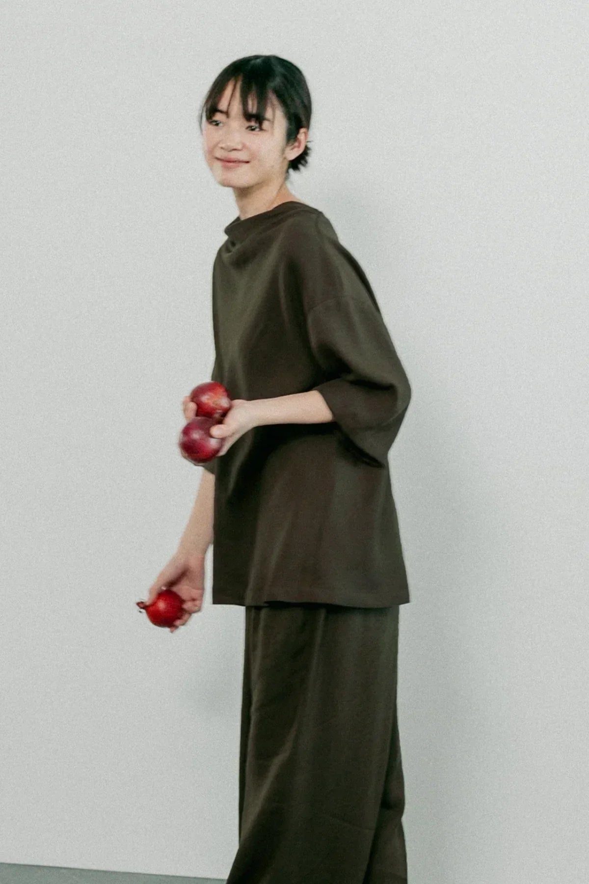 Smiling woman wearing loose brown loungewear holding red onions against plain white background