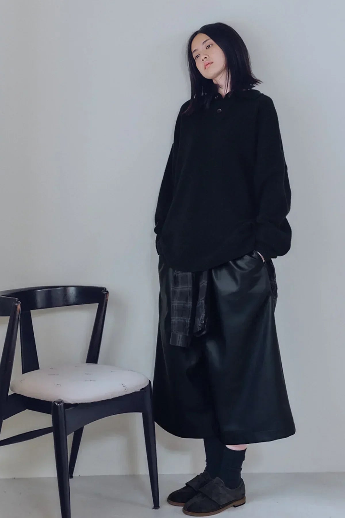 Woman wearing black oversized knit sweater and wide-leg leather pants standing by black chair