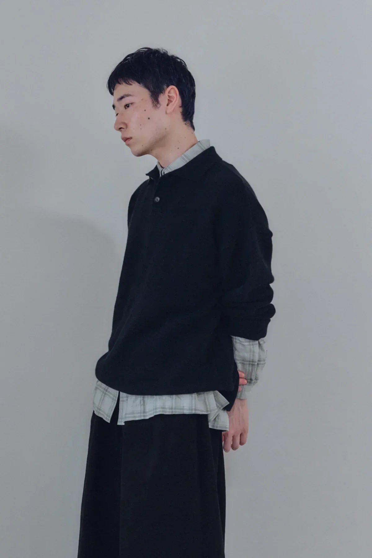 Profile of man wearing black knit Henley neck shirt over plaid shirt against plain background