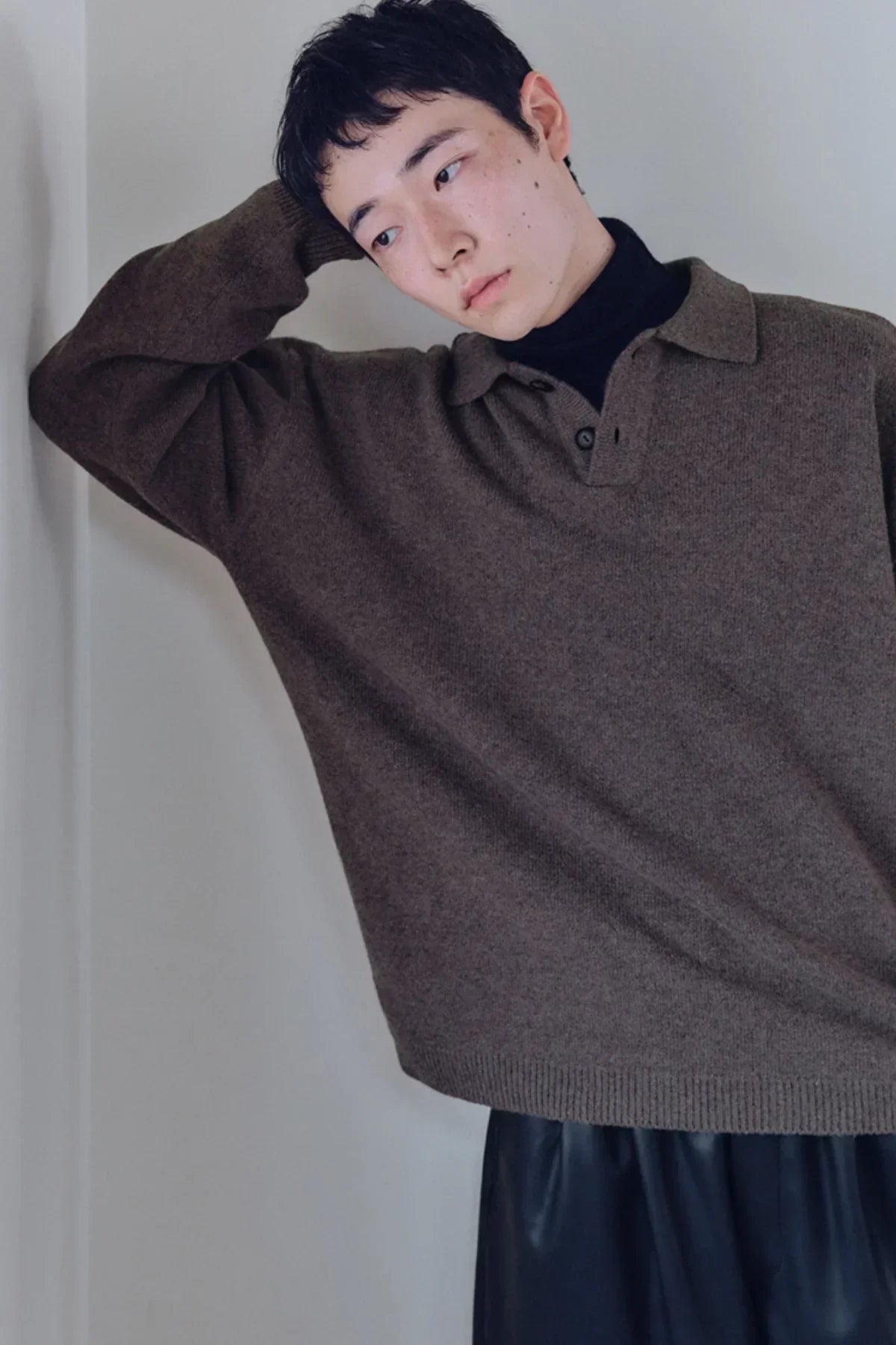 Close-up of a person wearing a brown knit henley-neck shirt over a black turtleneck, posing indoors