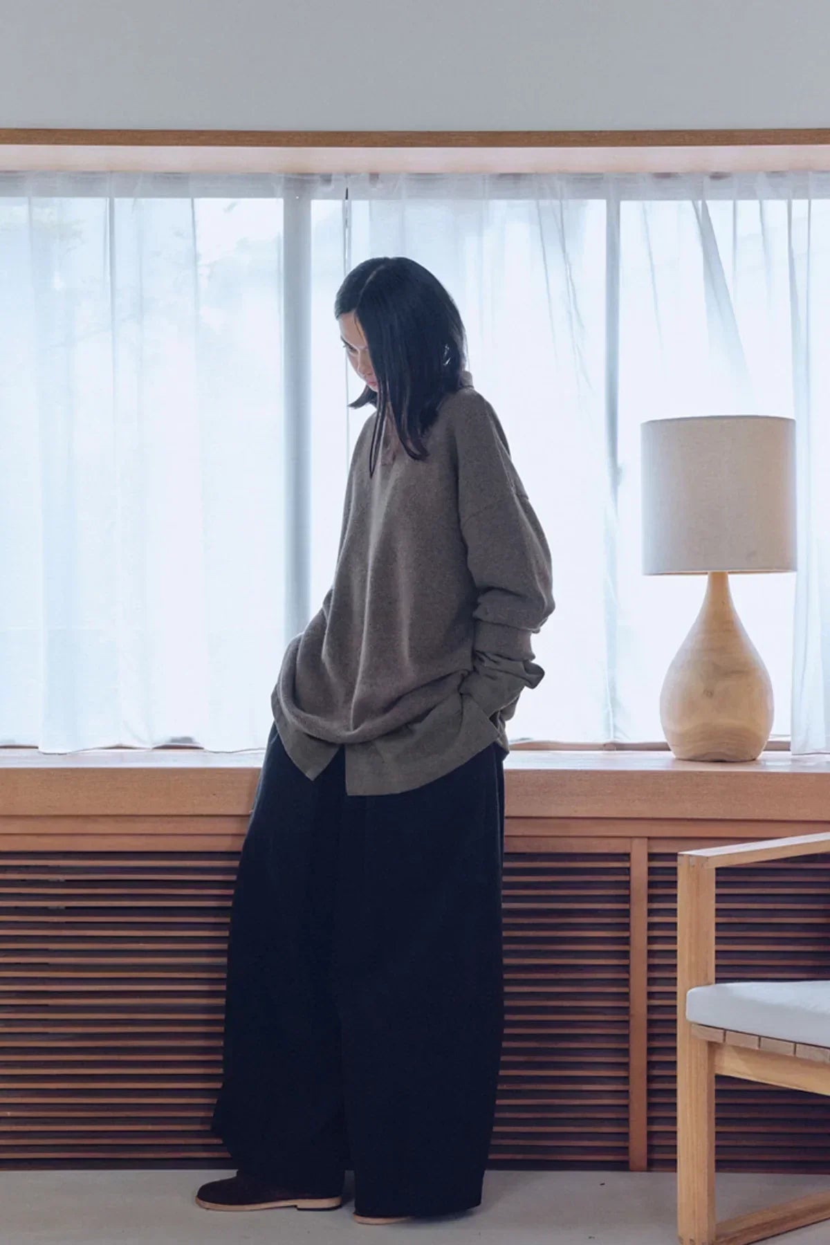 Model wearing brown oversized unisex knit Henley neck shirt and wide-leg black pants indoors