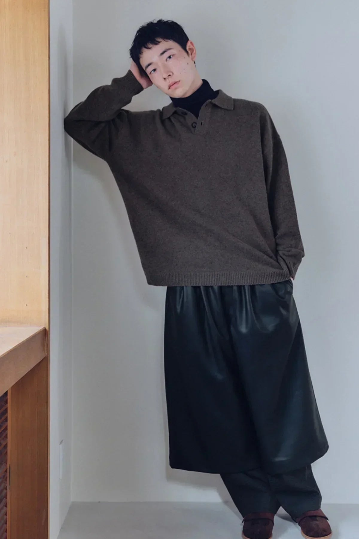 Model wearing brown knit henley neck shirt layered over black turtleneck with loose black pants indoors