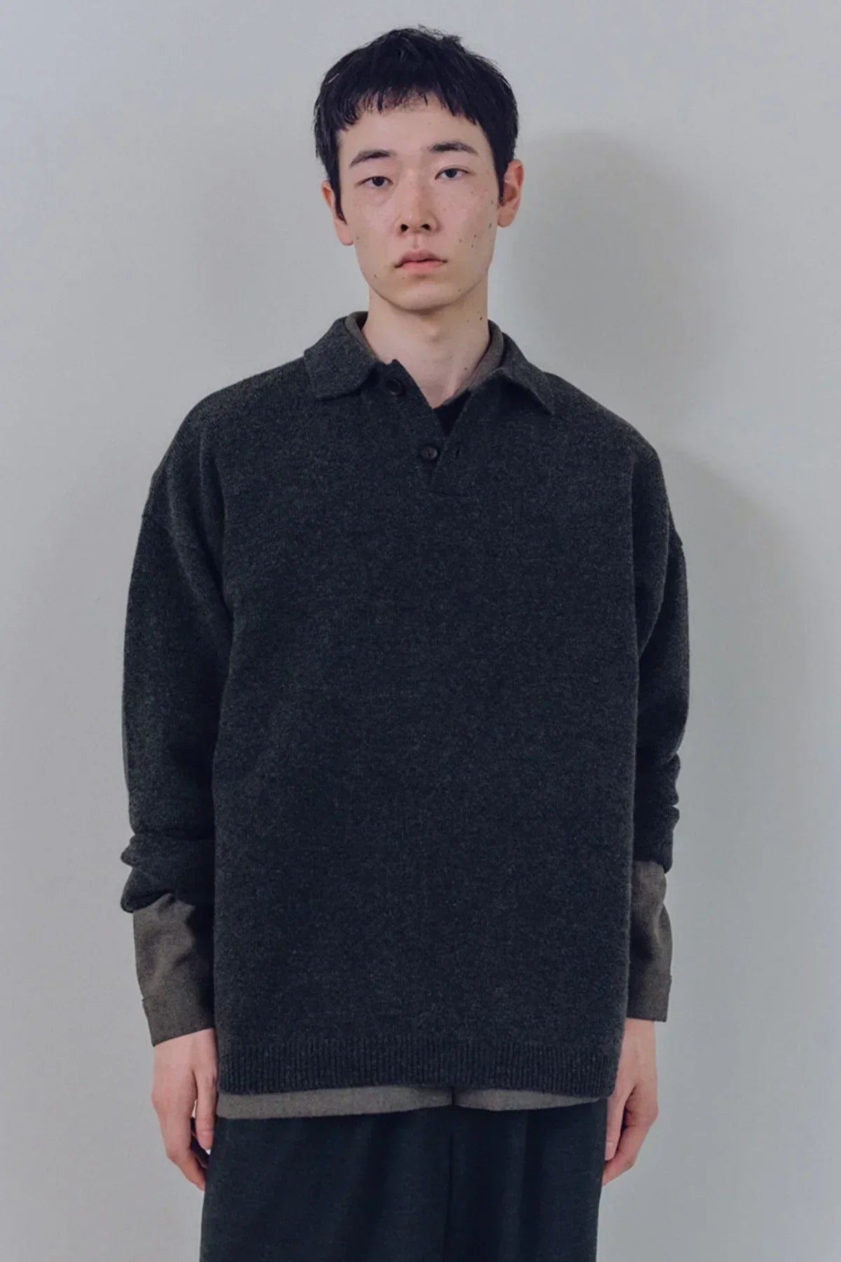 Model wearing charcoal unisex knit Henley-neck sweater over charcoal shirt in minimal studio setting