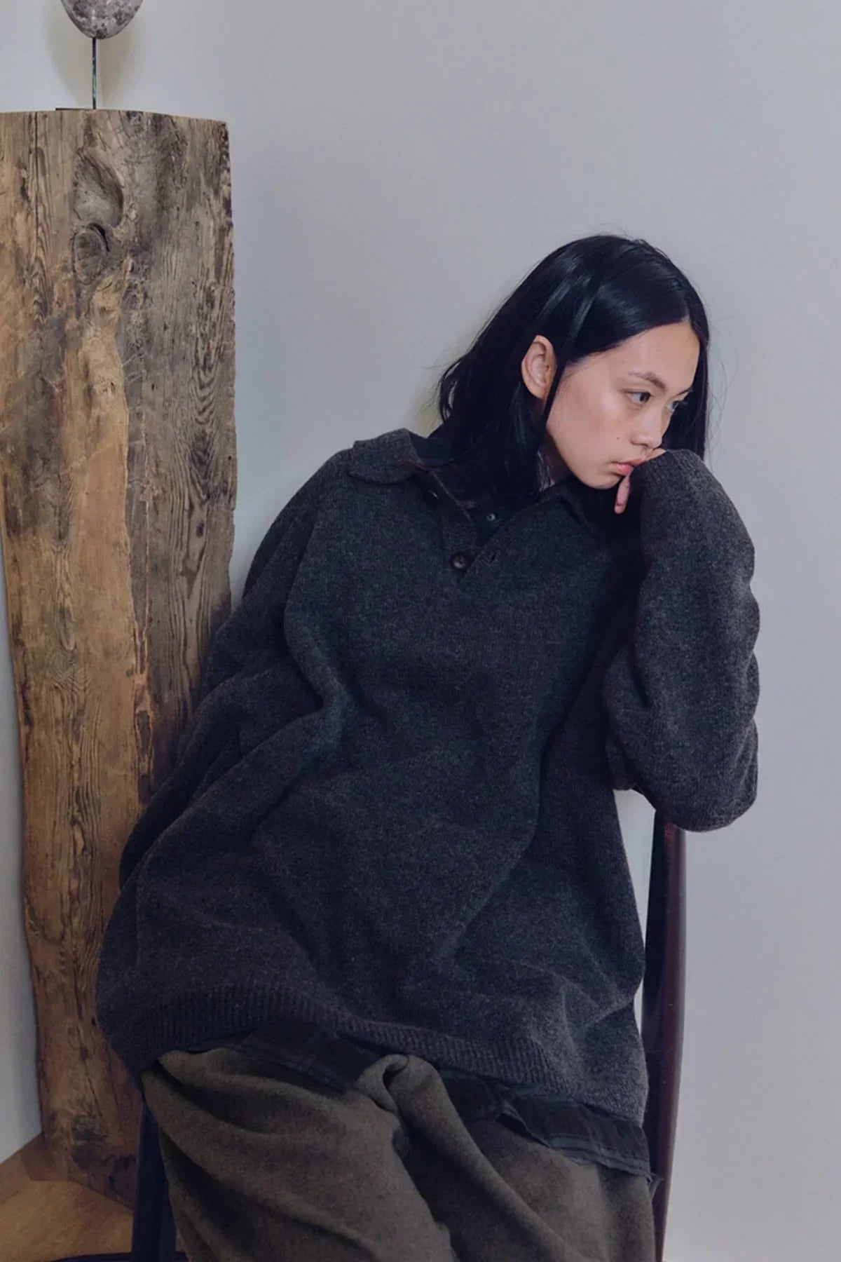 Model wearing charcoal unisex knit Henley neck shirt sitting indoors by wooden decor