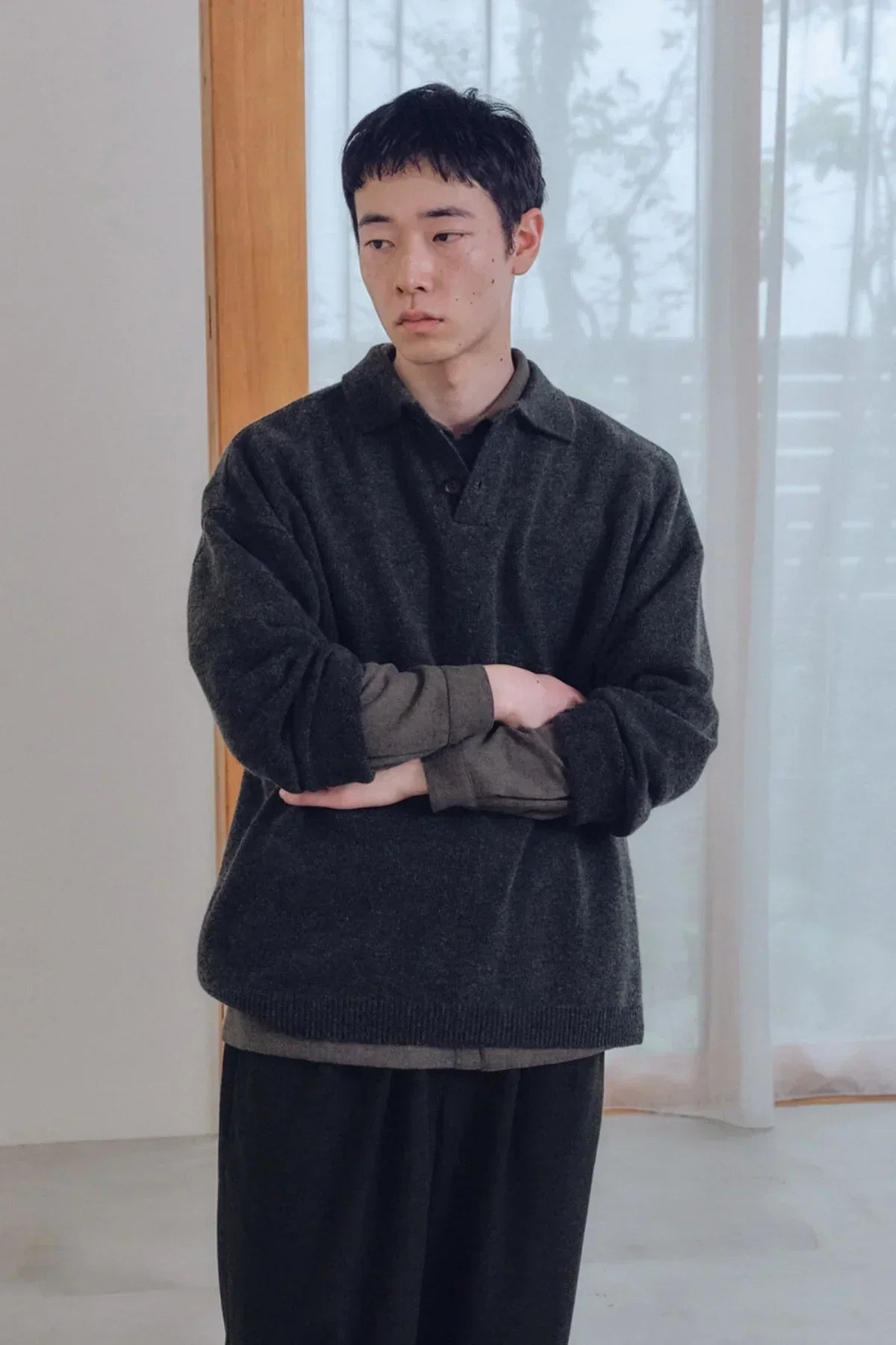 Young man wearing charcoal knit Henley neck shirt layered over long sleeve indoors with wooden window frame