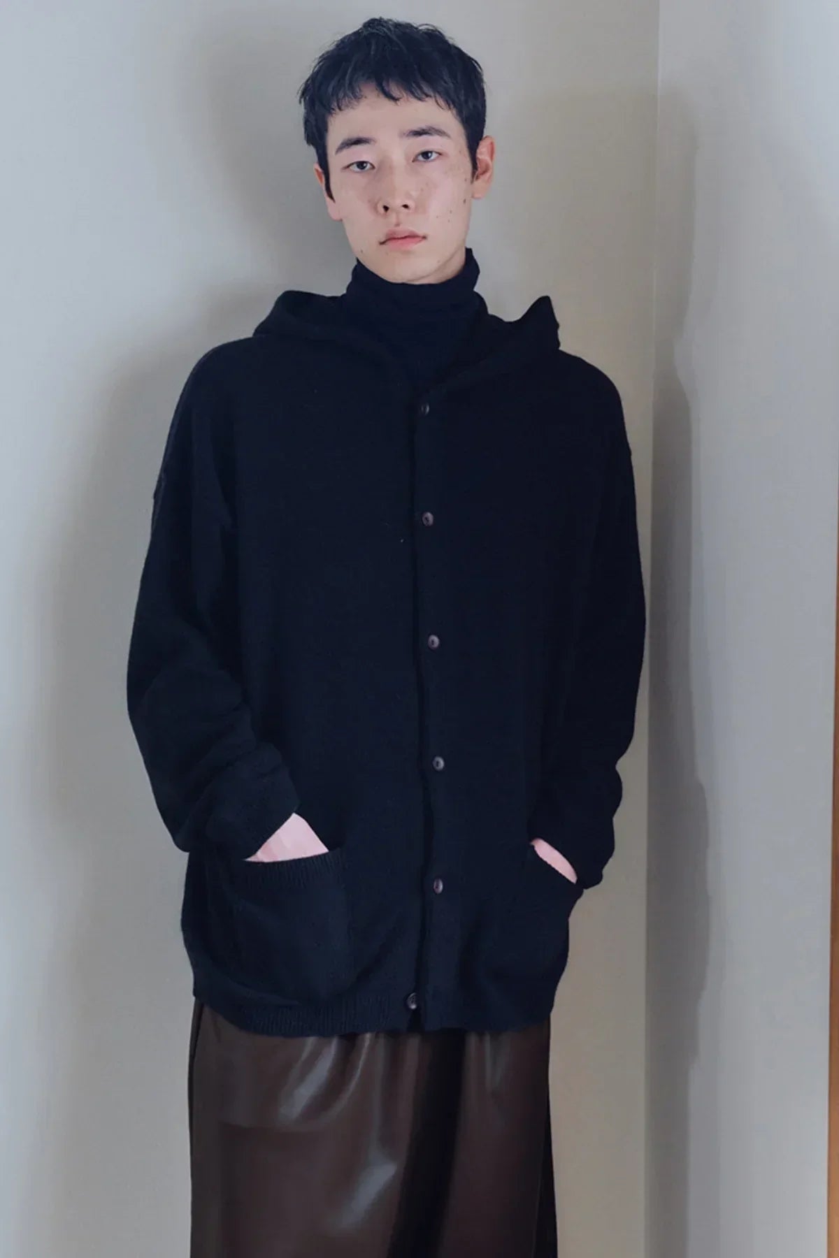 Model wearing black button-up knit hoodie and black turtleneck with brown leather pants