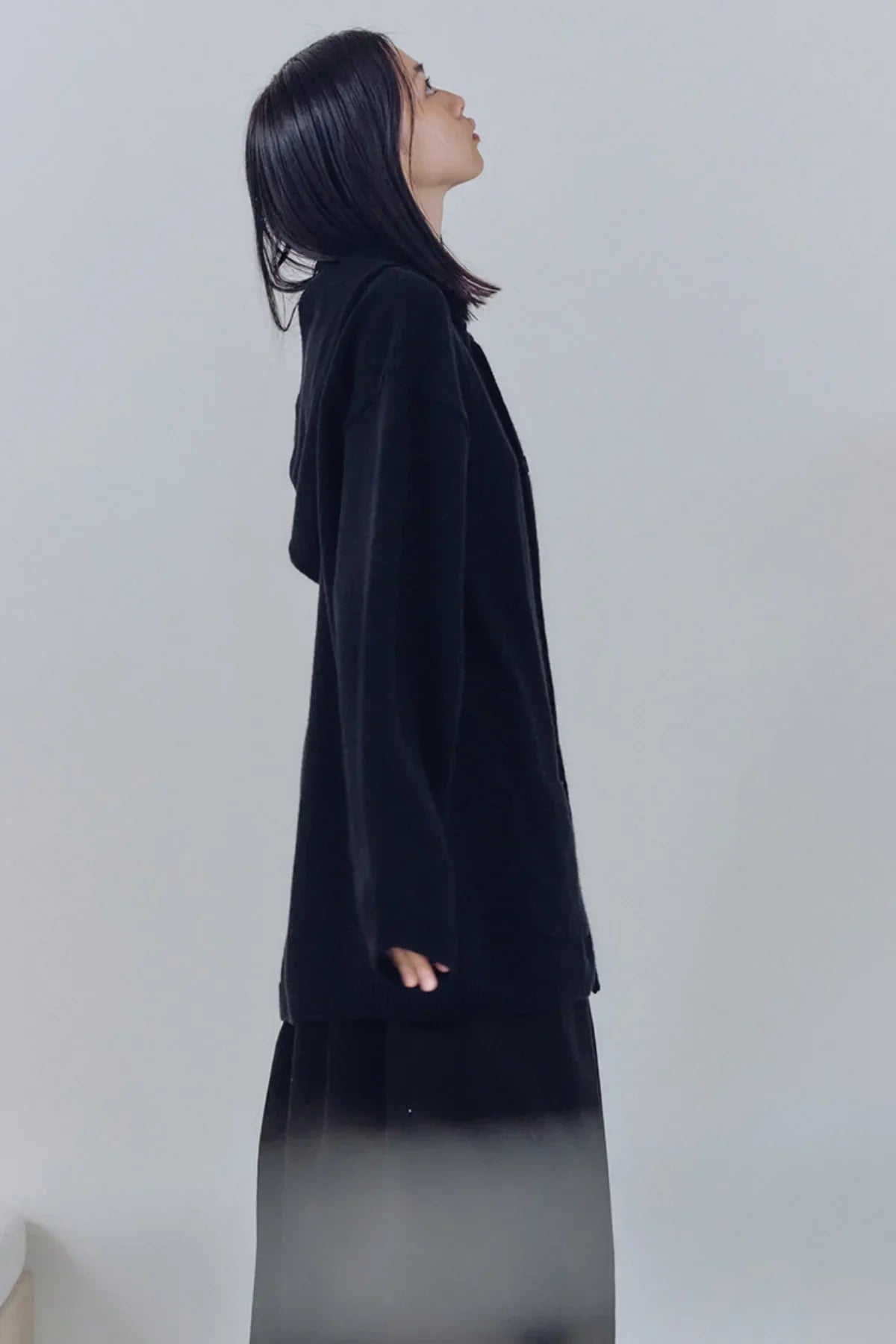 Side profile of person wearing black unisex knit hooded sweater against plain background