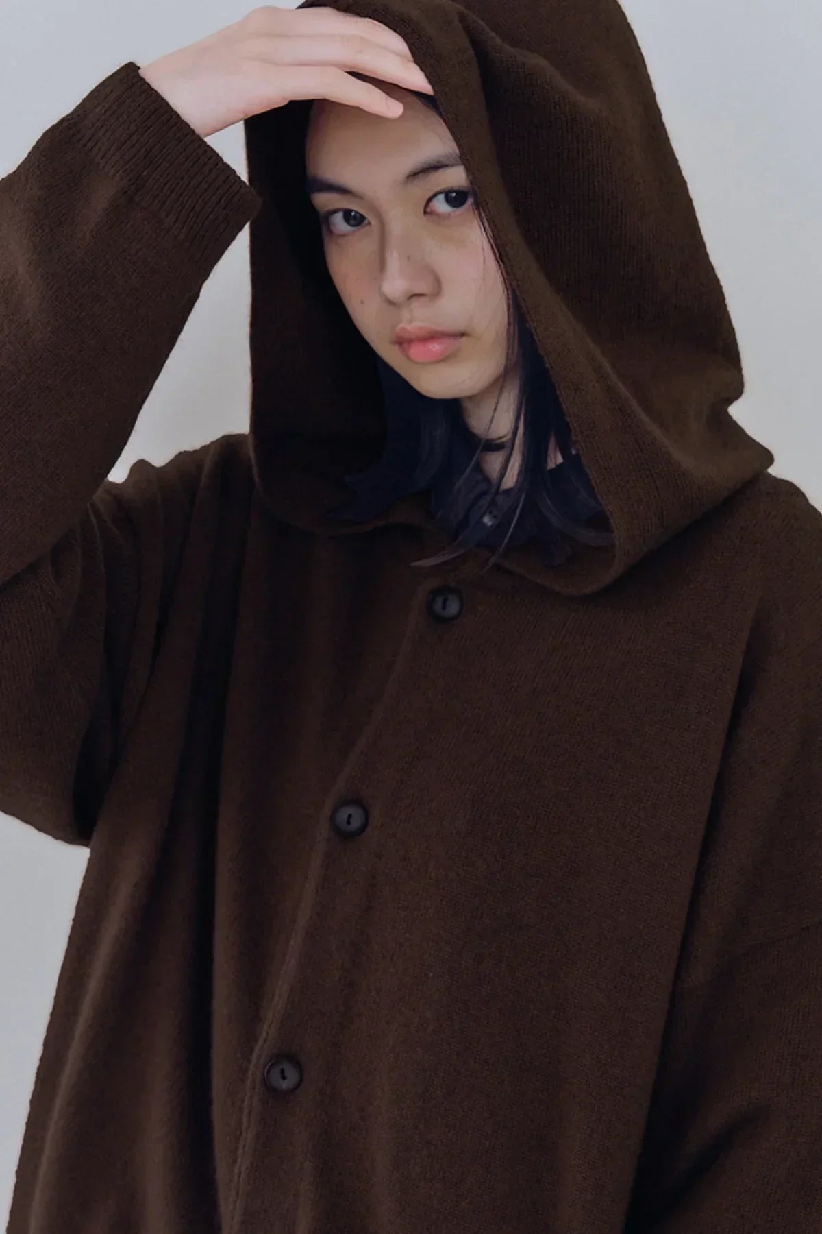 Close-up of a person wearing a brown unisex knit hooded cardigan with buttons