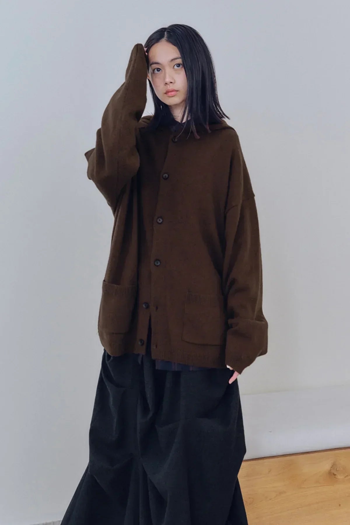 Young woman wearing oversized brown knit cardigan with buttons and black wide pants in minimal indoor setting