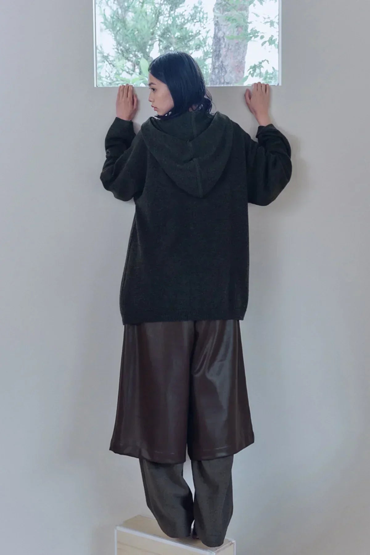Model wearing oversized dark knit hooded sweater and brown leather wide-leg shorts indoors