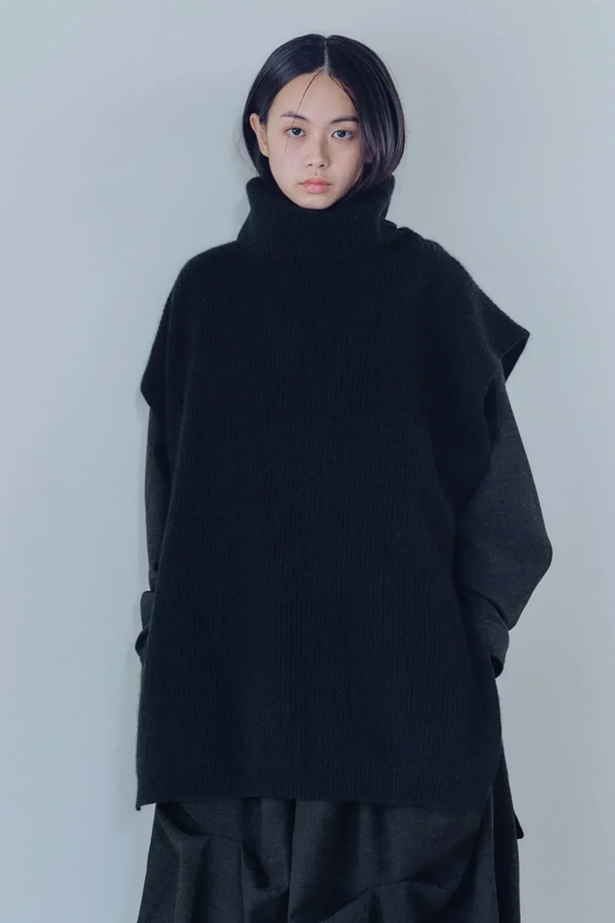 Asian woman wearing black knit turtleneck vest over dark long sleeves against plain background