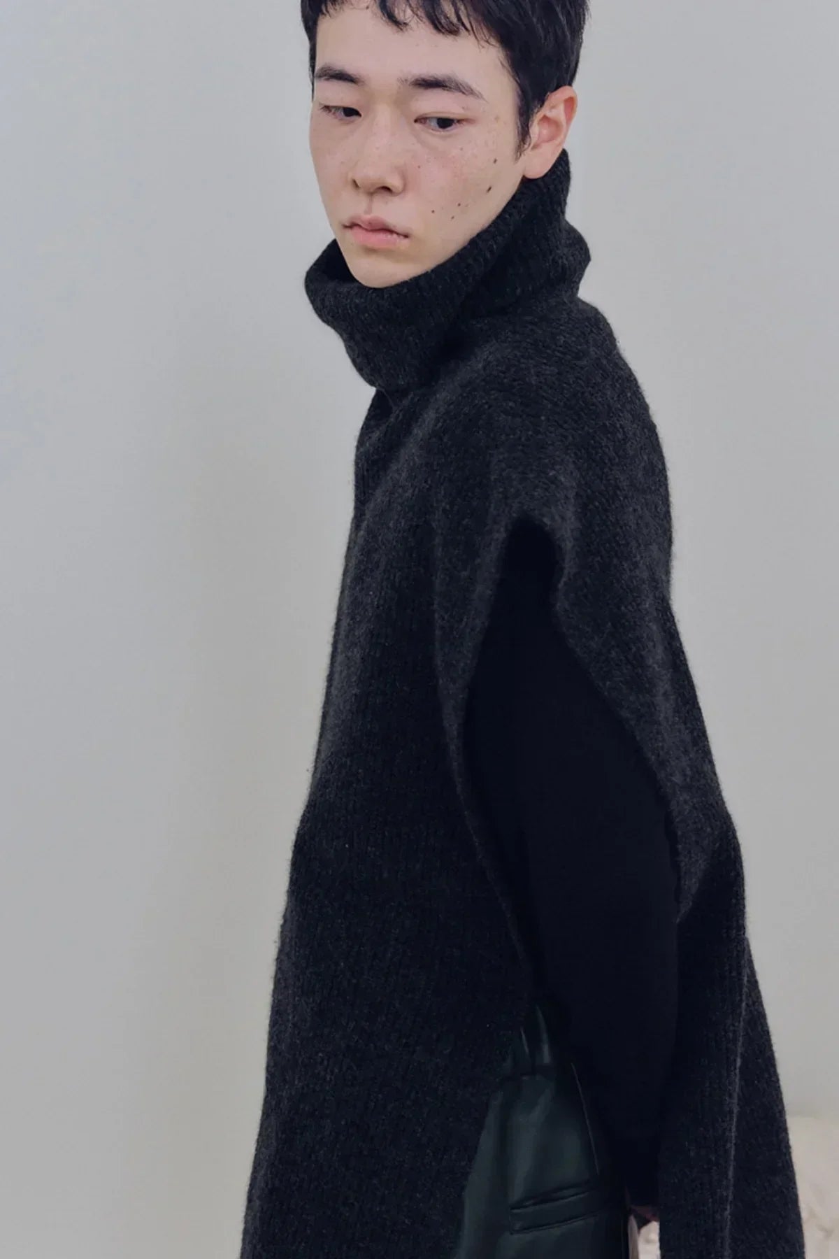 Close-up of a person wearing a charcoal knit sleeveless turtleneck vest over a black long sleeve top
