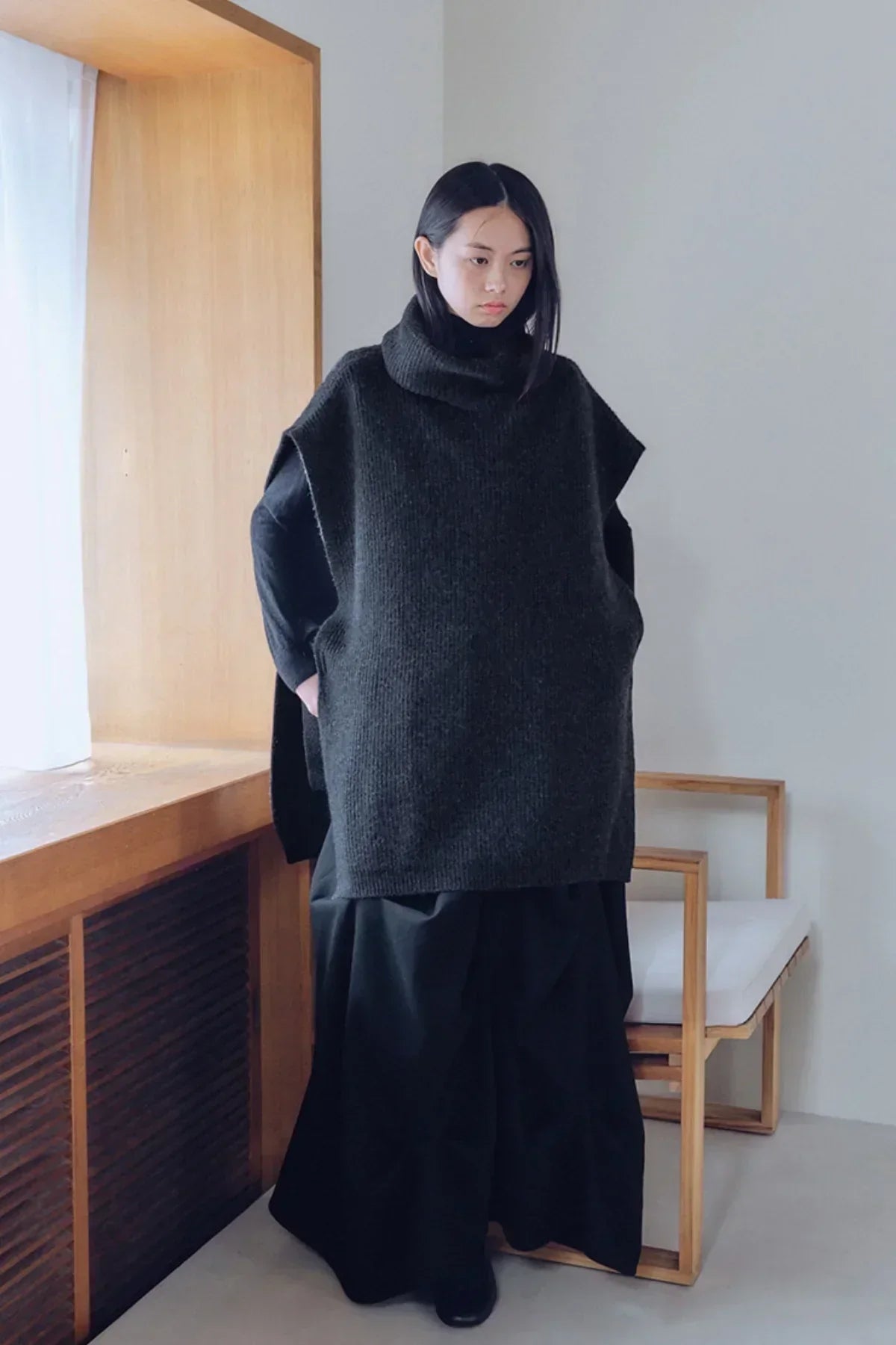 model wearing charcoal unisex knit turtleneck vest with black long sleeves and wide pants indoors