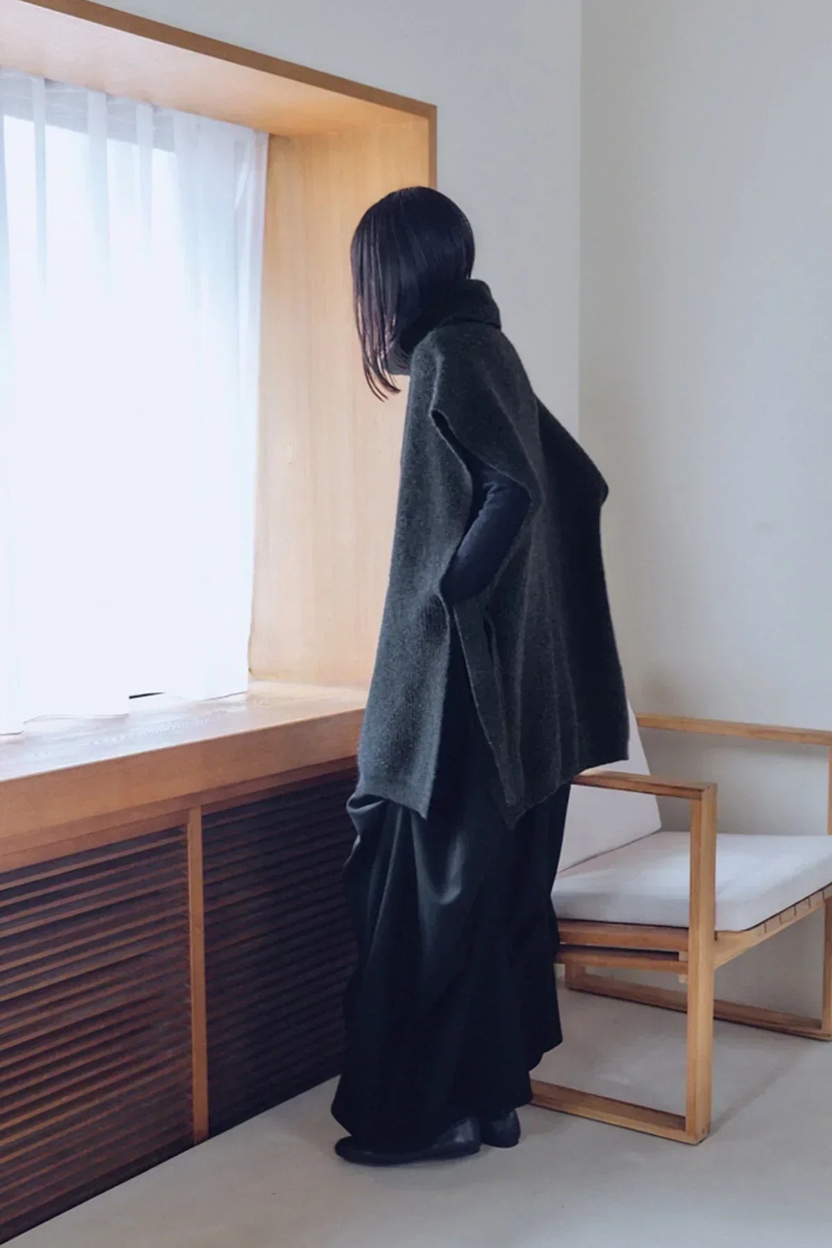 Person wearing charcoal knit sleeveless turtleneck vest indoors by window with wooden chair