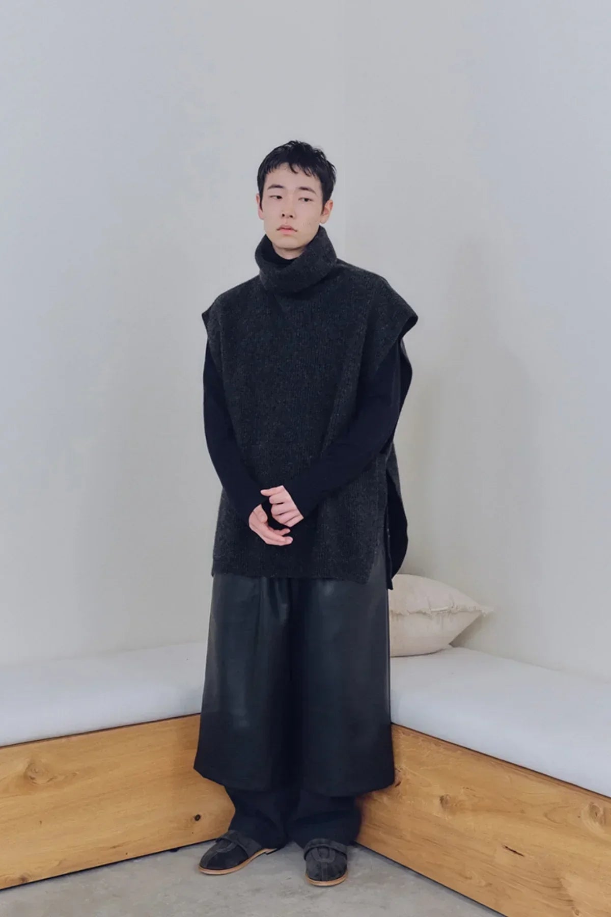 Model wearing charcoal knit sleeveless turtleneck vest with black wide leather pants in minimalist room