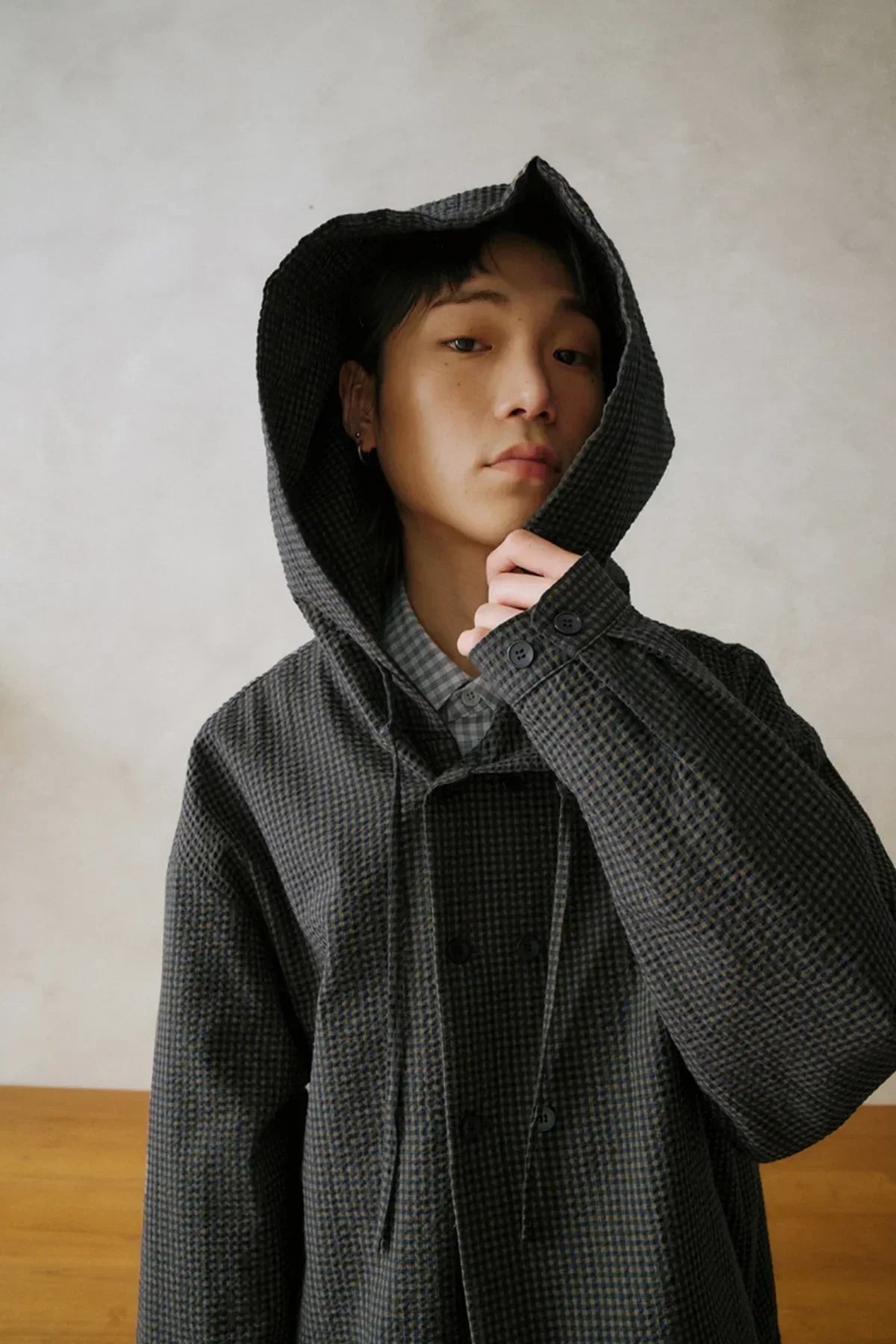 Person wearing dark checkered seersucker hooded jacket with double-breasted buttons indoors