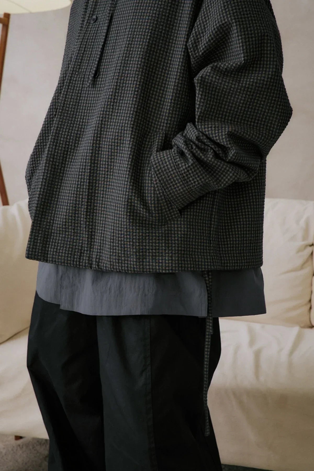 Close-up of person wearing dark checkered jacket with hands in pockets, layered over gray shirt and black pants