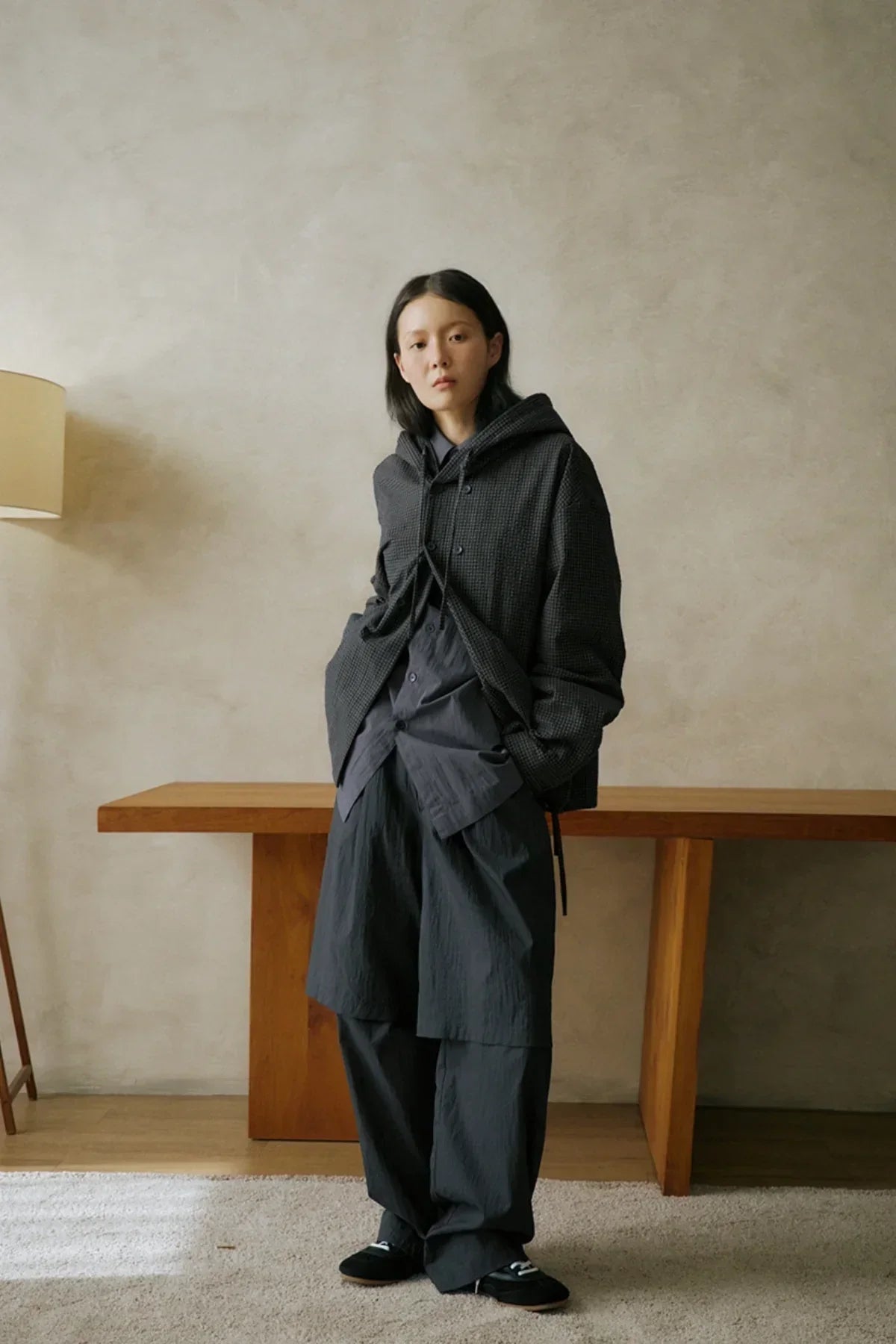 Woman wearing loose dark gray layered outfit and textured hooded jacket standing indoors