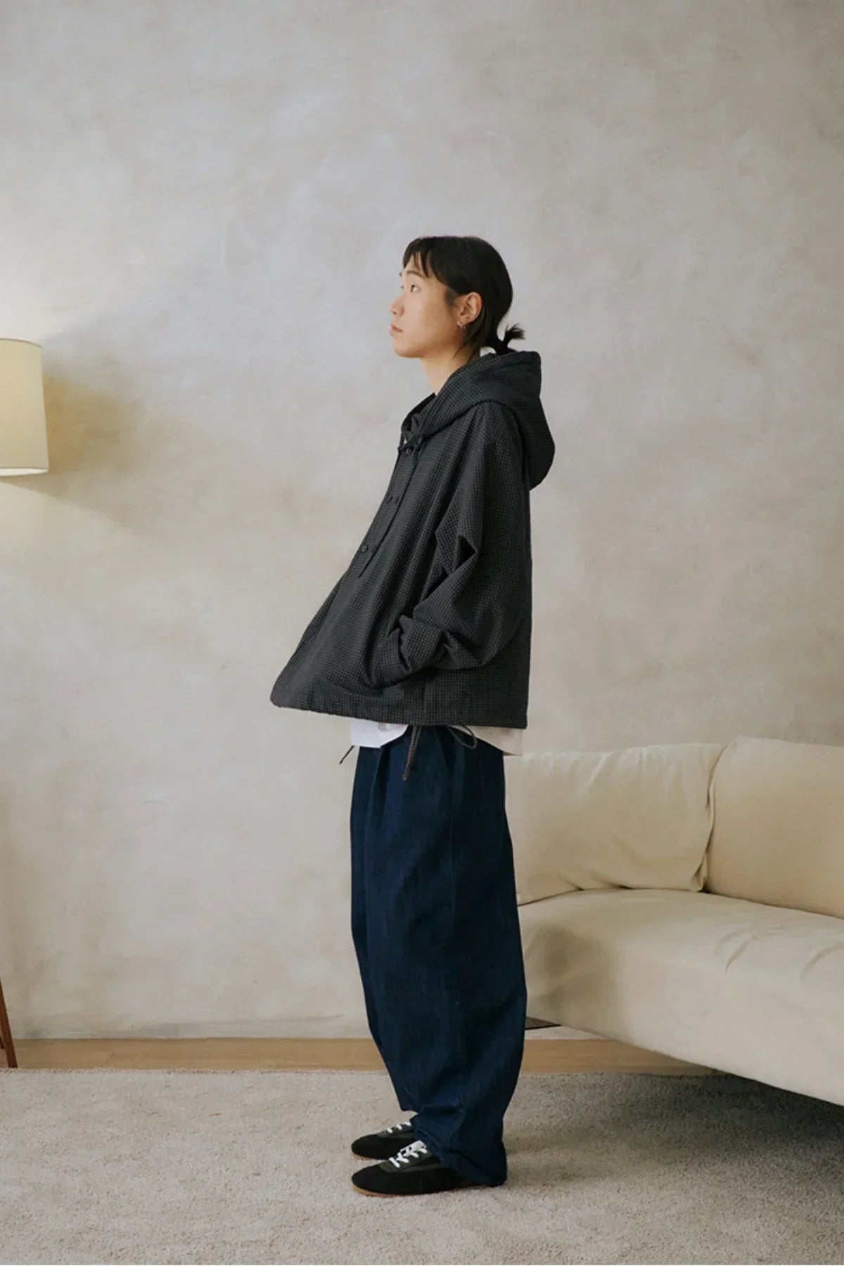 Side view of person wearing loose dark checkered hooded jacket and wide blue pants indoors