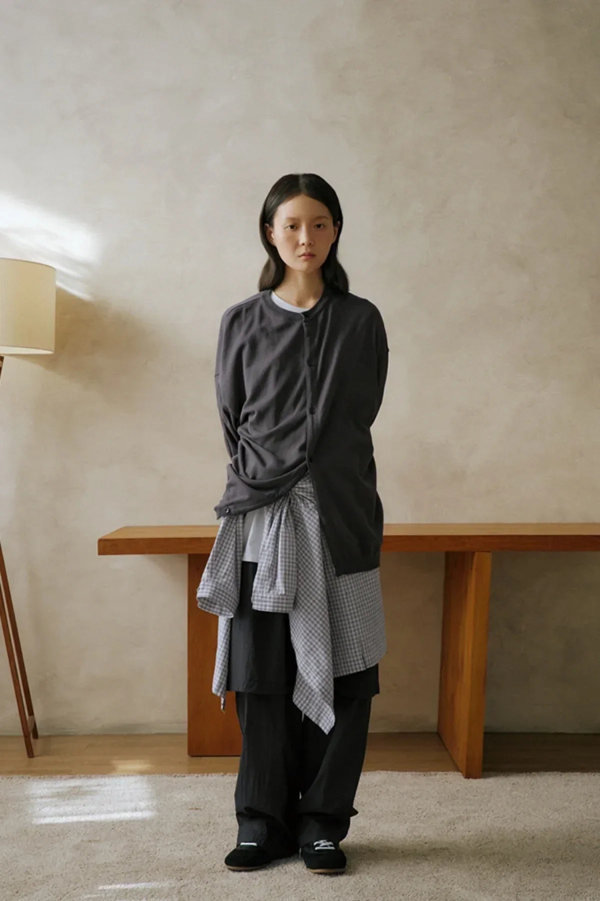 Model wearing gray layered see-through unisex pants with oversized cardigan and checkered shirt indoors