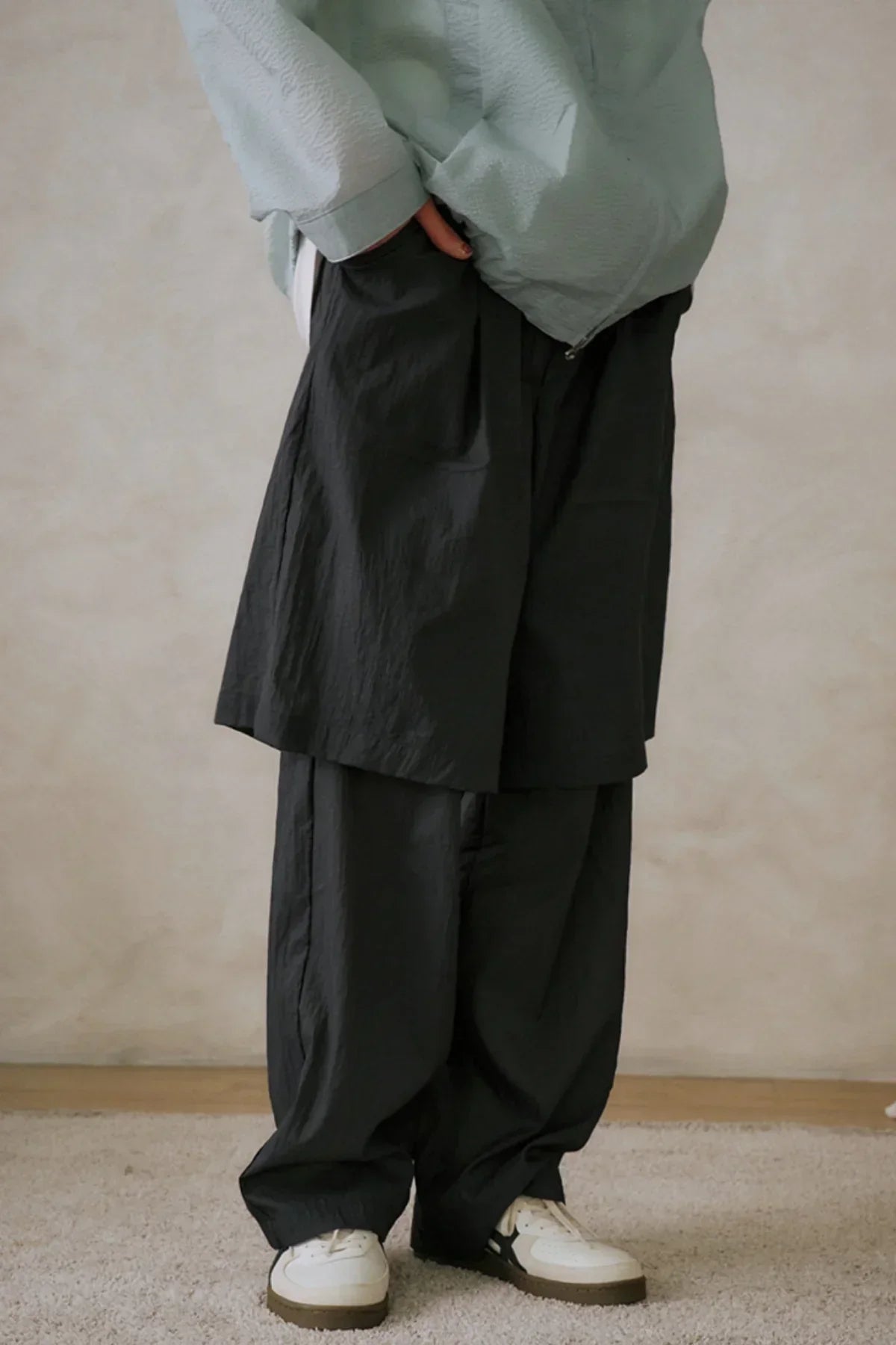 Person wearing black layered wide-leg pants with light green jacket and white sneakers in studio