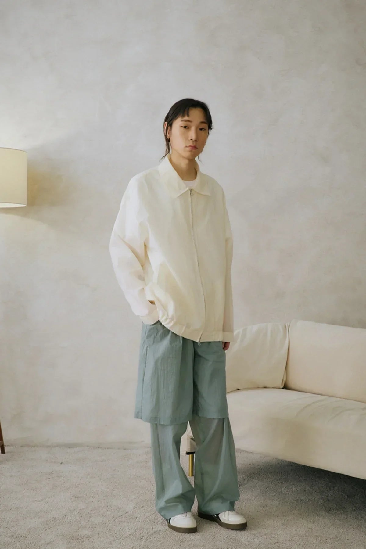 Model wearing mint layered unisex pants with white jacket and sneakers in minimalist living room