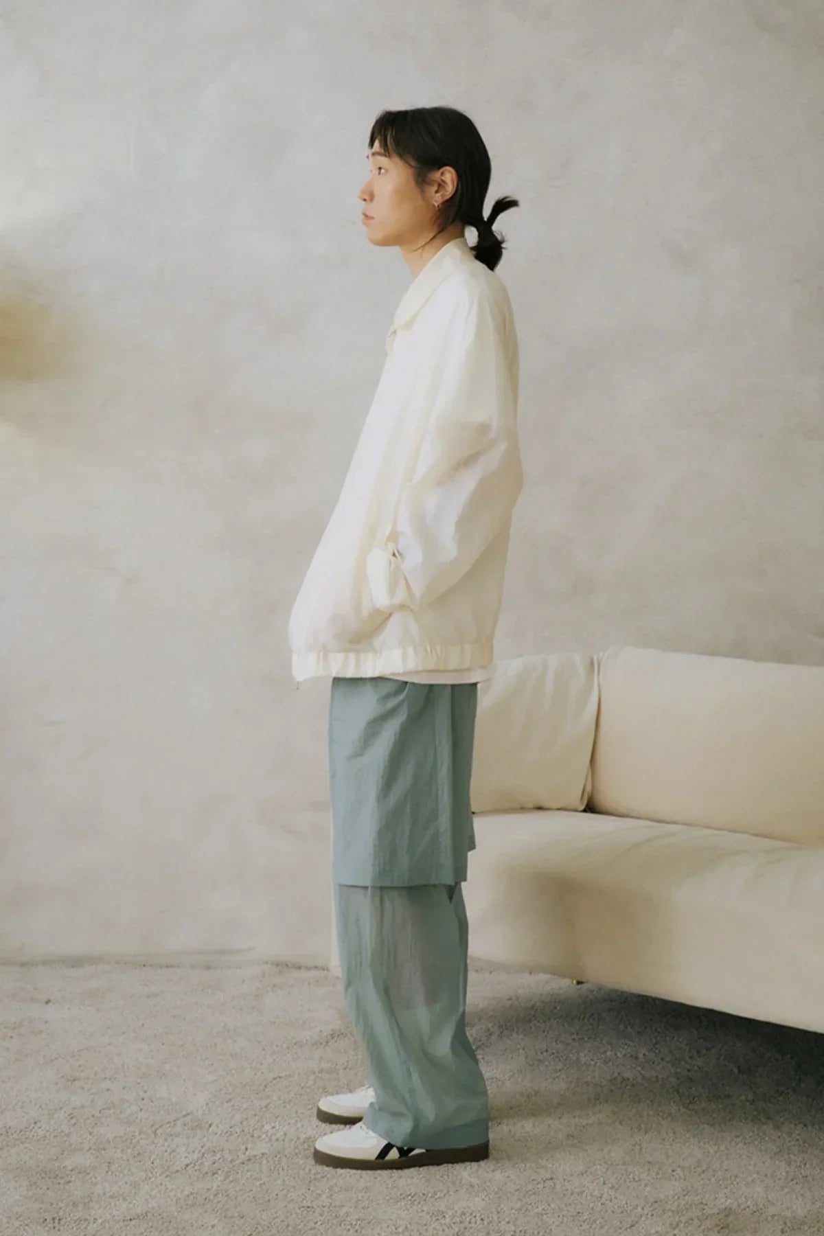 Side view of person wearing mint layered see-through pants with white jacket and sneakers indoors