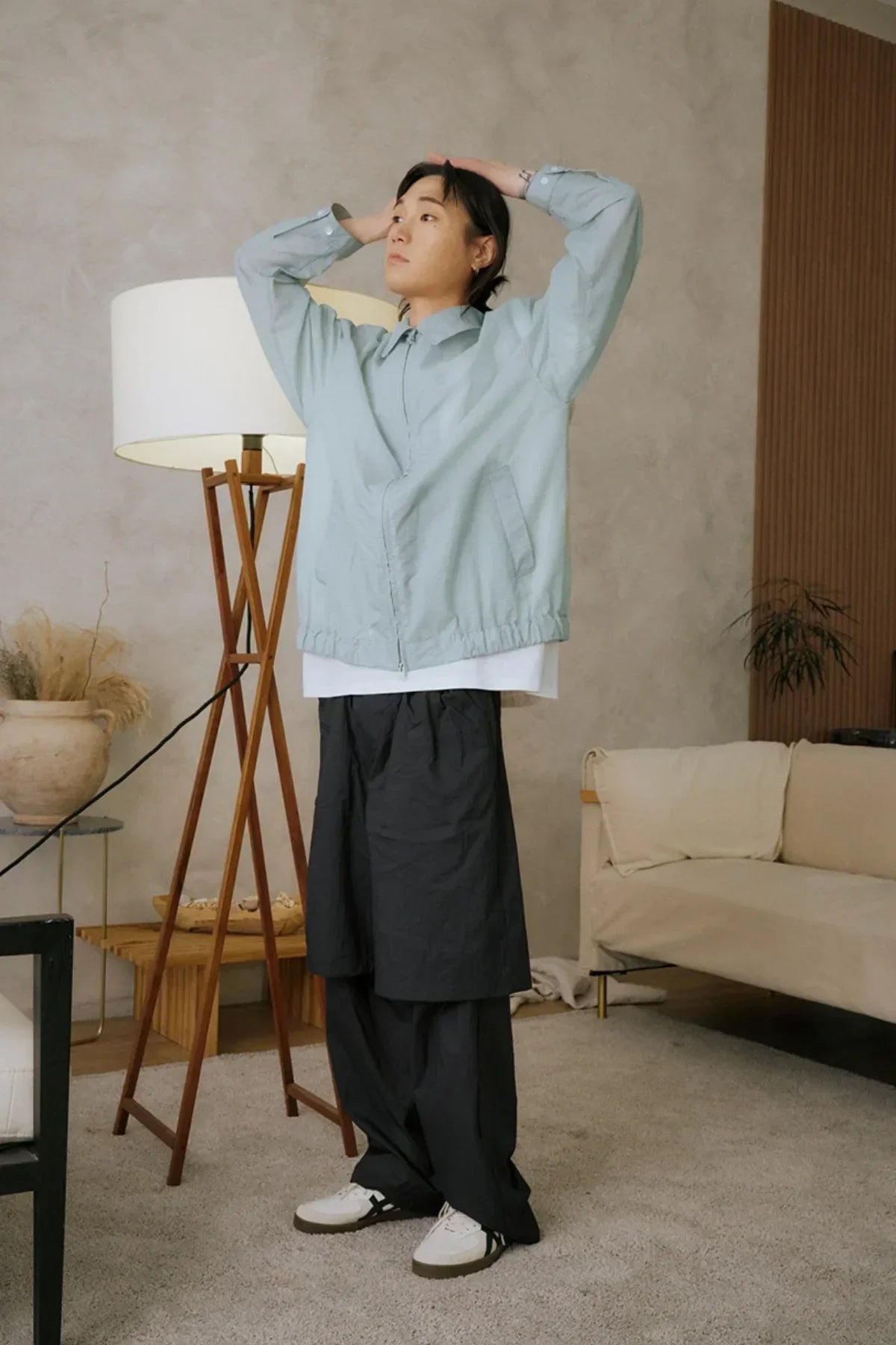 Model wearing unisex mint green jacket and black layered see-through pants in modern living room