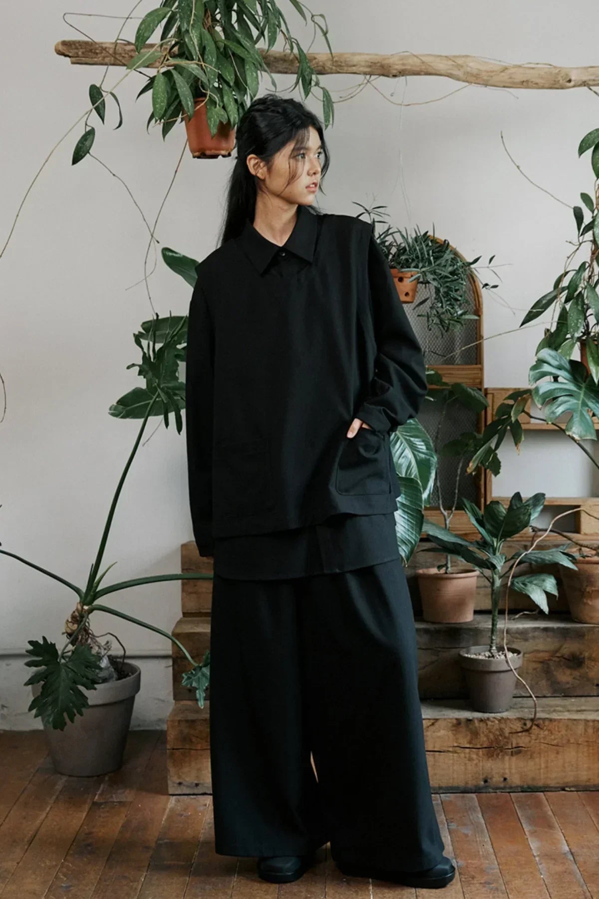 Woman wearing oversized black unisex shirt and wide-leg pants in indoor plant-filled setting