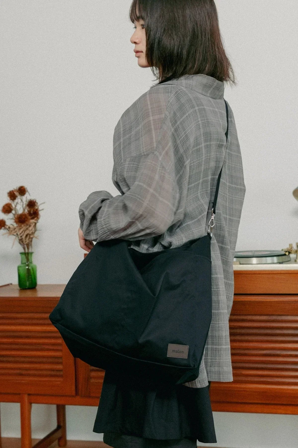 Side view of person wearing gray plaid shirt carrying large black unisex shoulder bag indoors