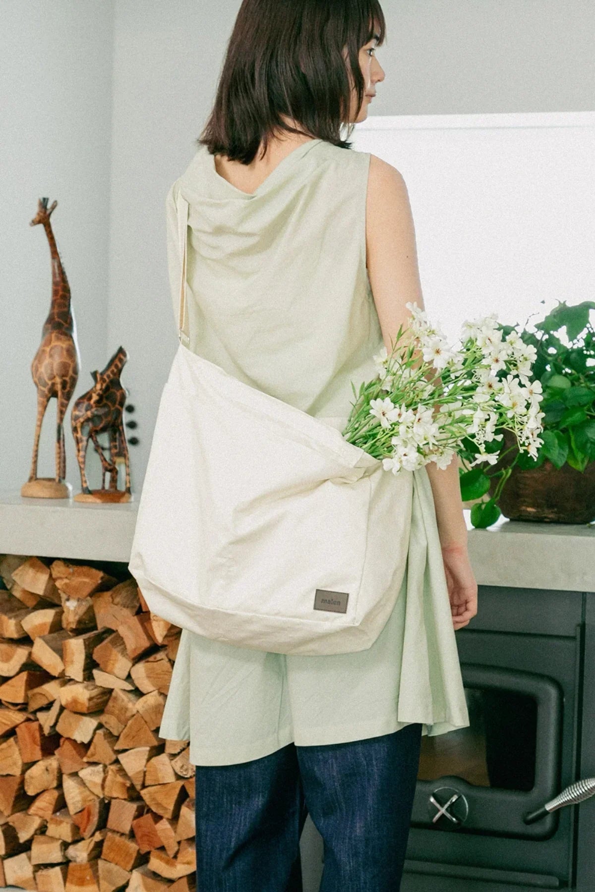 Woman in light green top carrying a cream unisex shoulder bag with white flowers indoors