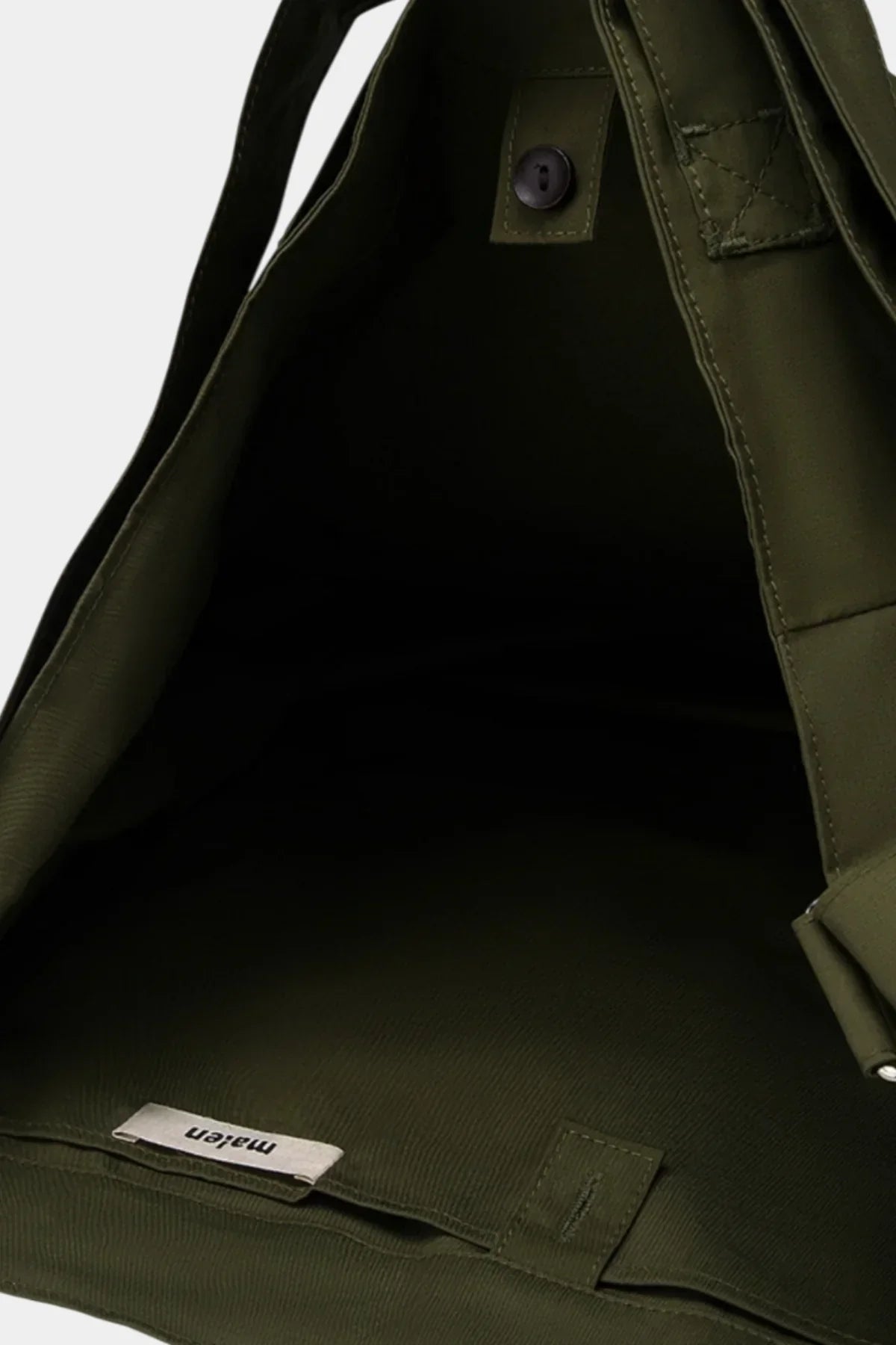 Close-up of interior of khaki unisex shoulder bag with button closure and fabric tag