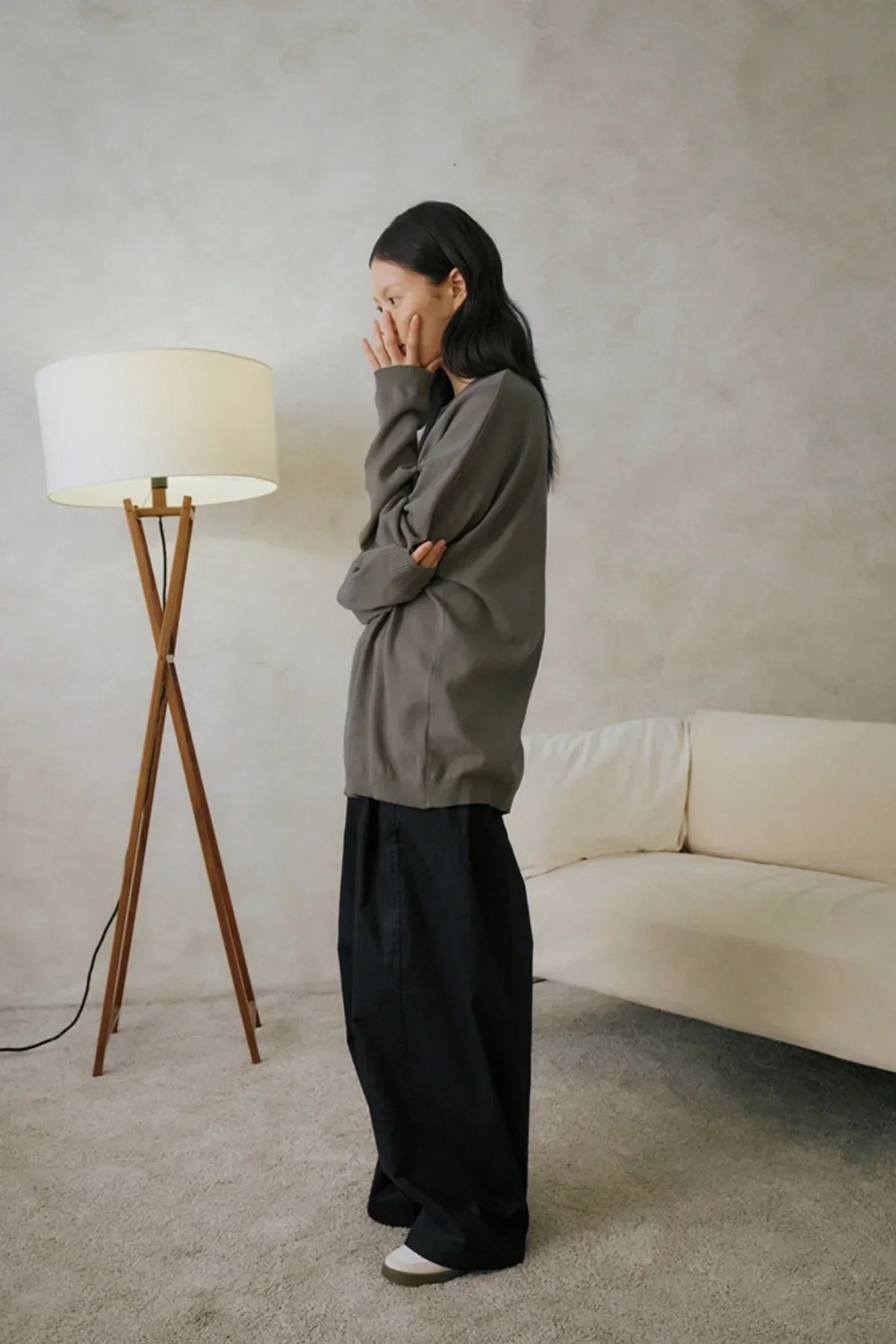 Side view of a woman wearing black wide-leg pants and an oversized olive sweater in a minimalist living room