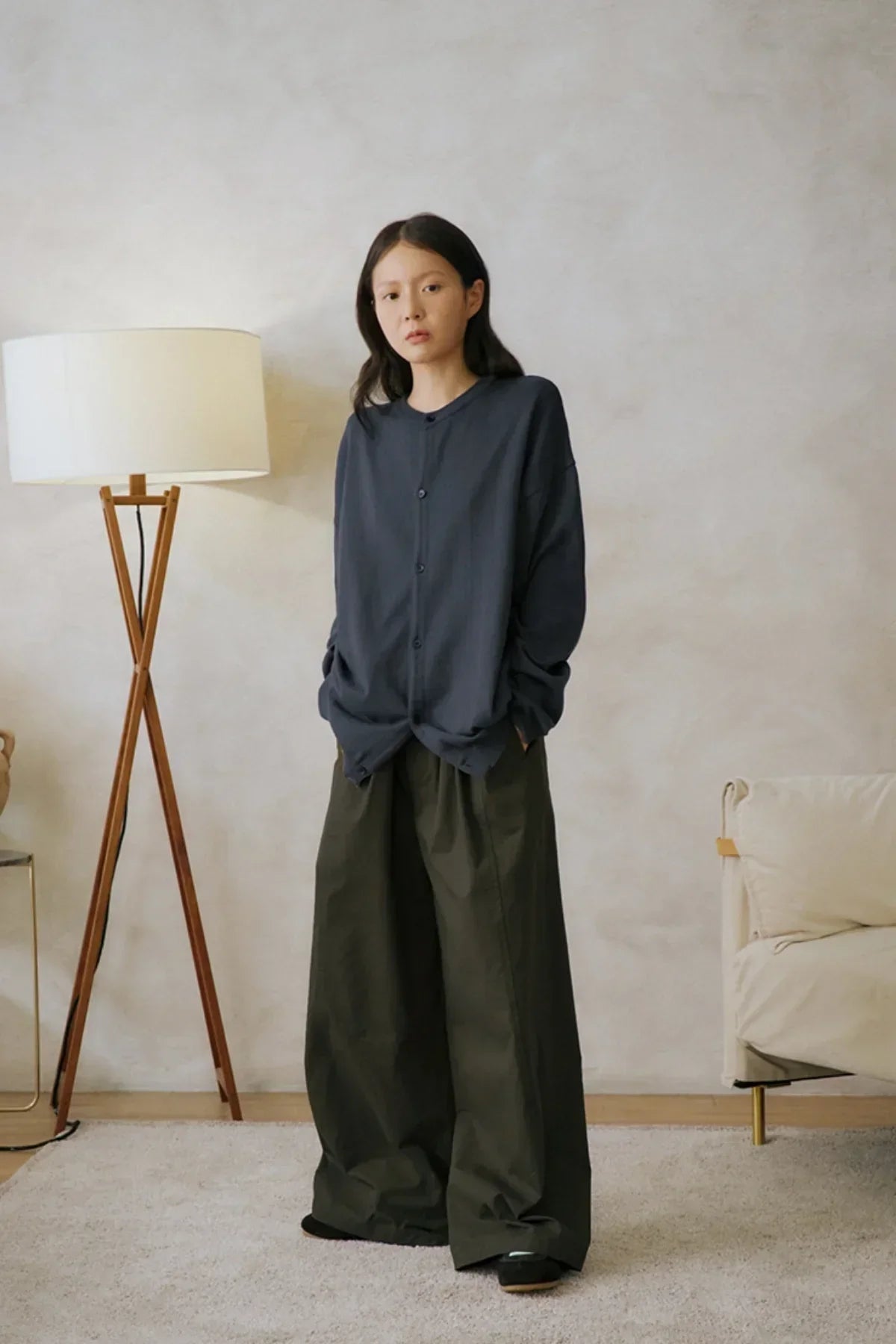 Woman wearing oversized black button-up shirt and wide-leg khaki pants in minimalist living room