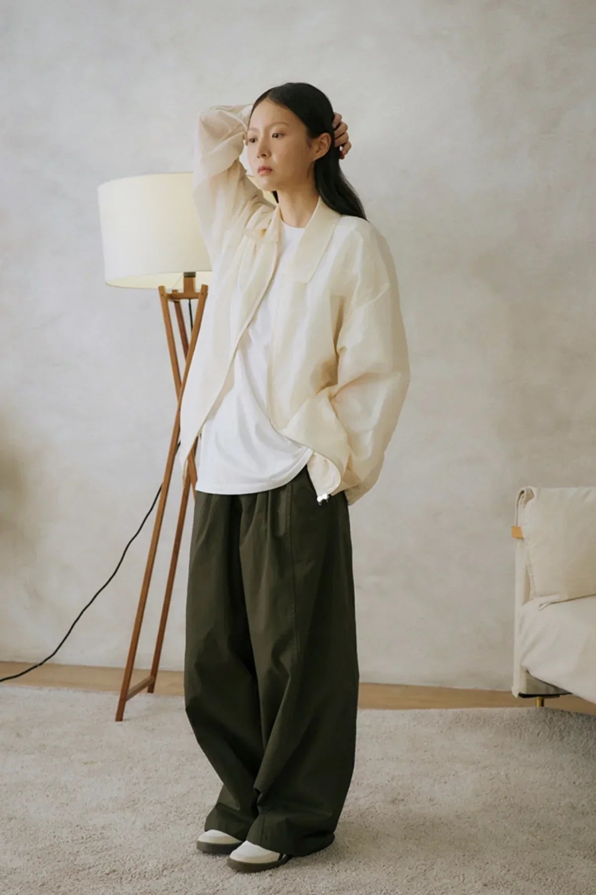Woman wearing oversized white jacket and khaki wide-leg pants standing in minimalist living room