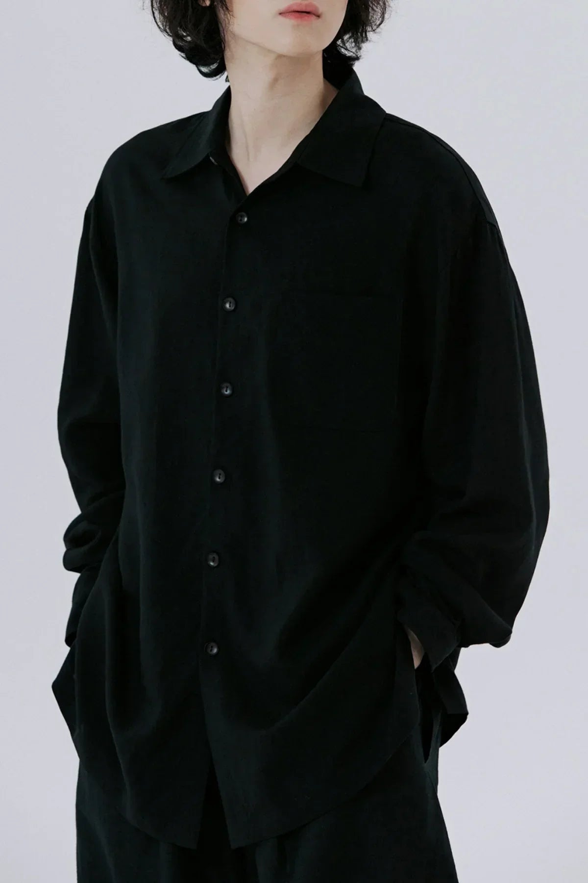 Close-up of a person wearing a loose-fitting black button-up shirt with long sleeves and a chest pocket