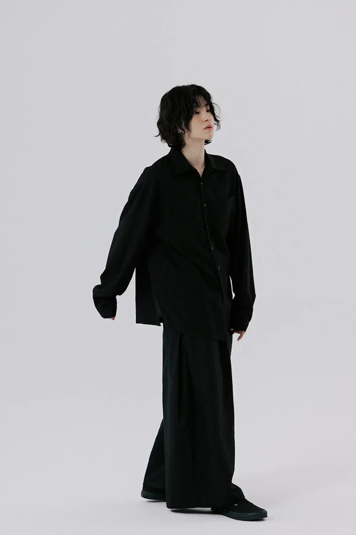 Model wearing oversized black button-up shirt and wide-leg black pants on plain background