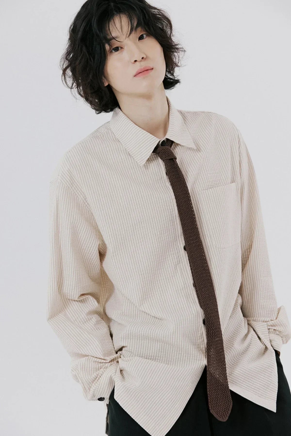 Person wearing a beige striped unisex shirt with a brown knit tie against plain white background