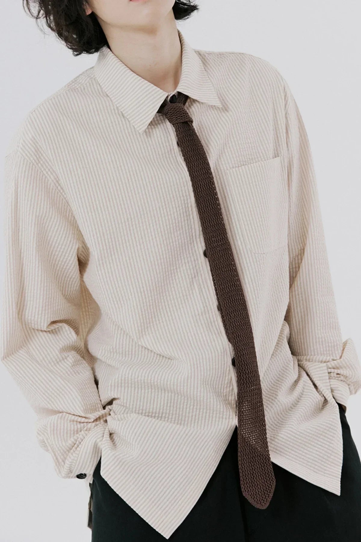 Close-up of person wearing beige striped shirt and dark knitted tie with hands in pockets