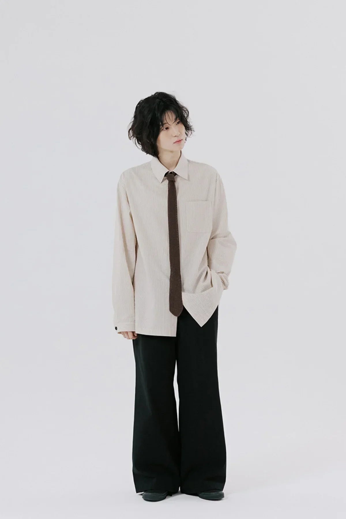 Person wearing beige striped shirt with brown tie and black wide-leg pants on white background
