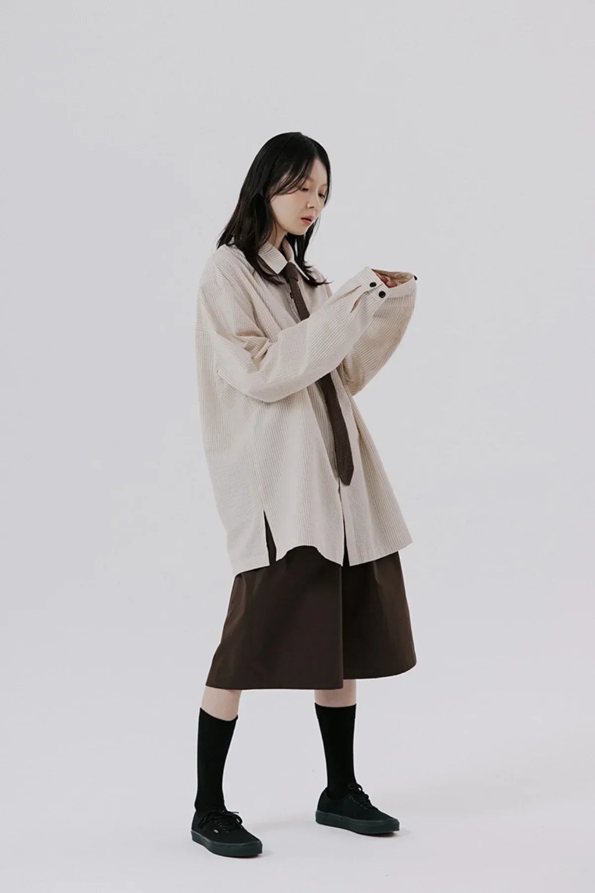 Model wearing beige oversized striped shirt with brown tie and shorts, black socks, and sneakers