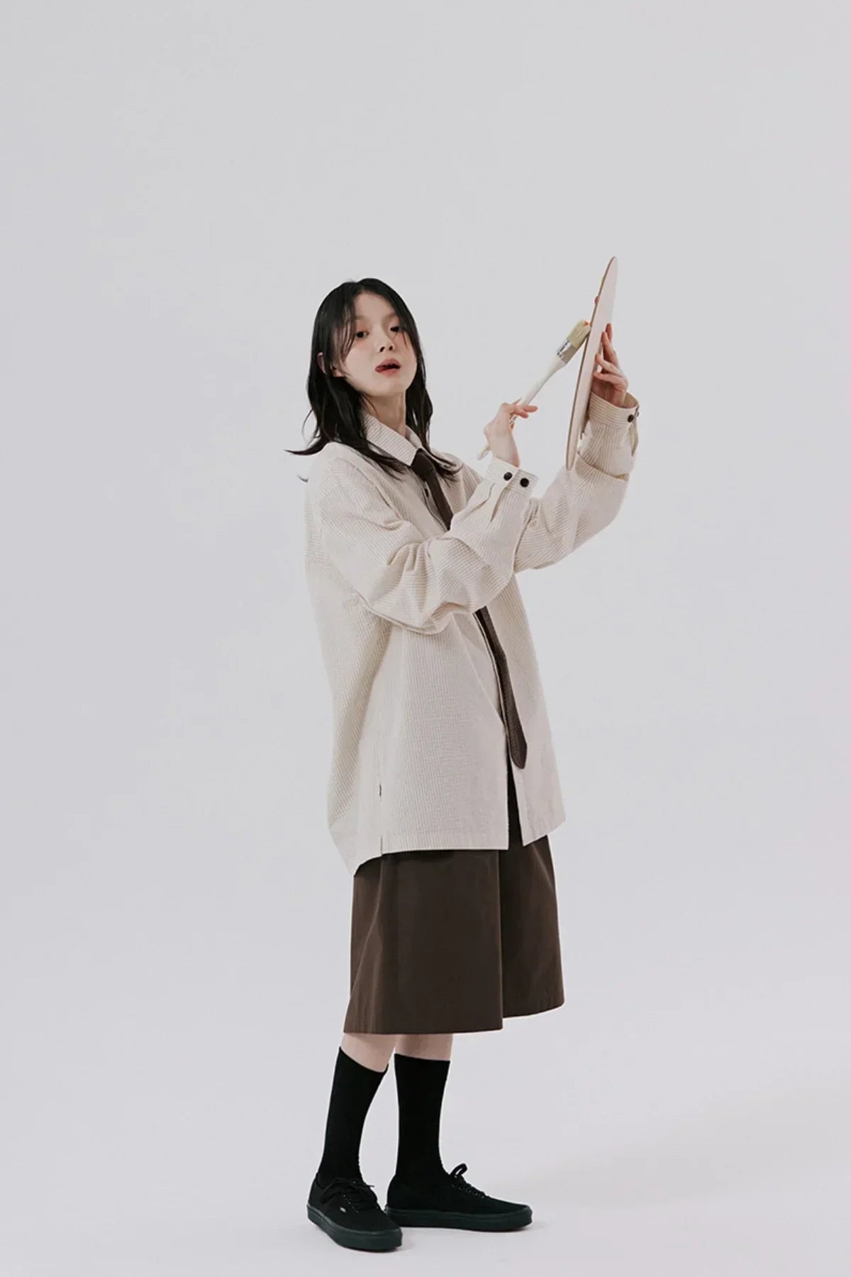 Young woman in beige oversized shirt and brown shorts painting on canvas in studio