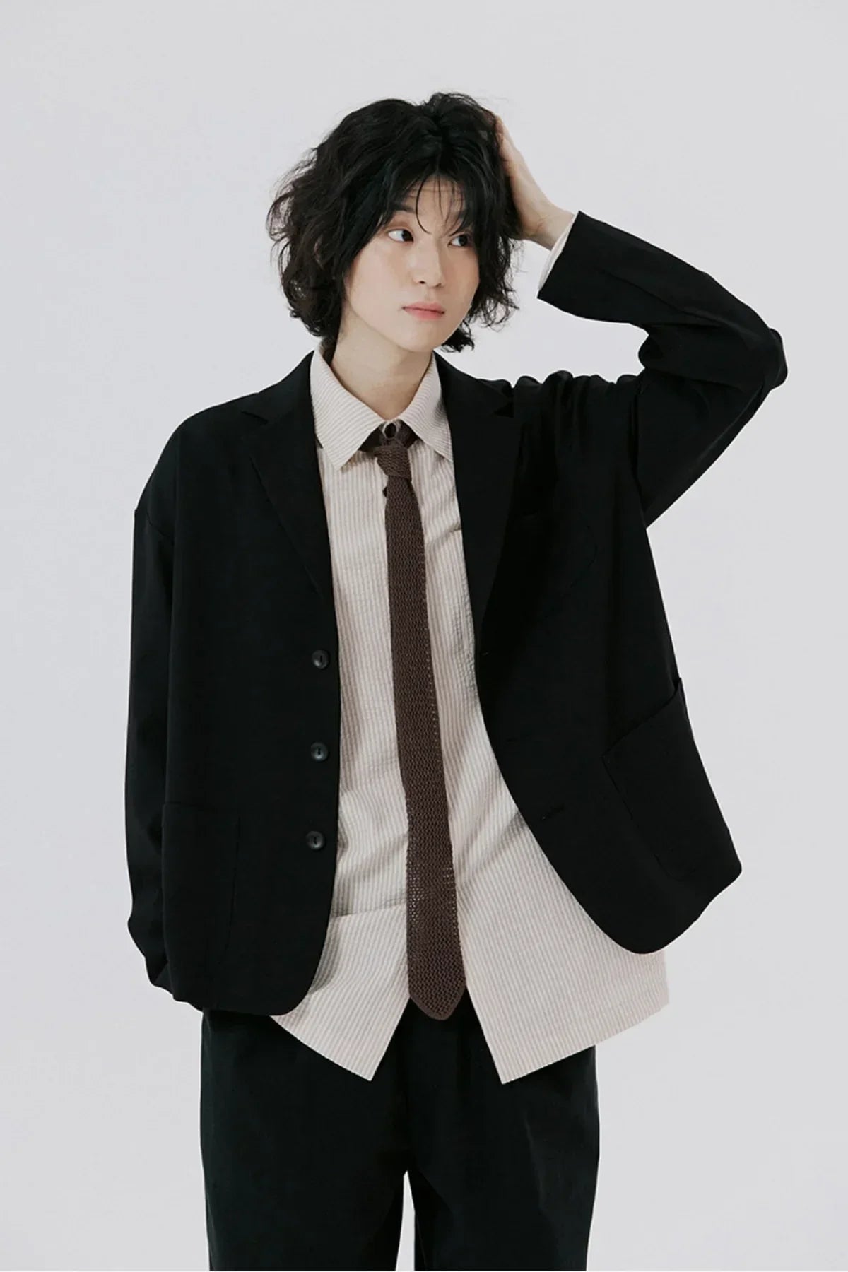 Portrait of person wearing black blazer, beige shirt, brown knit tie posing on white background